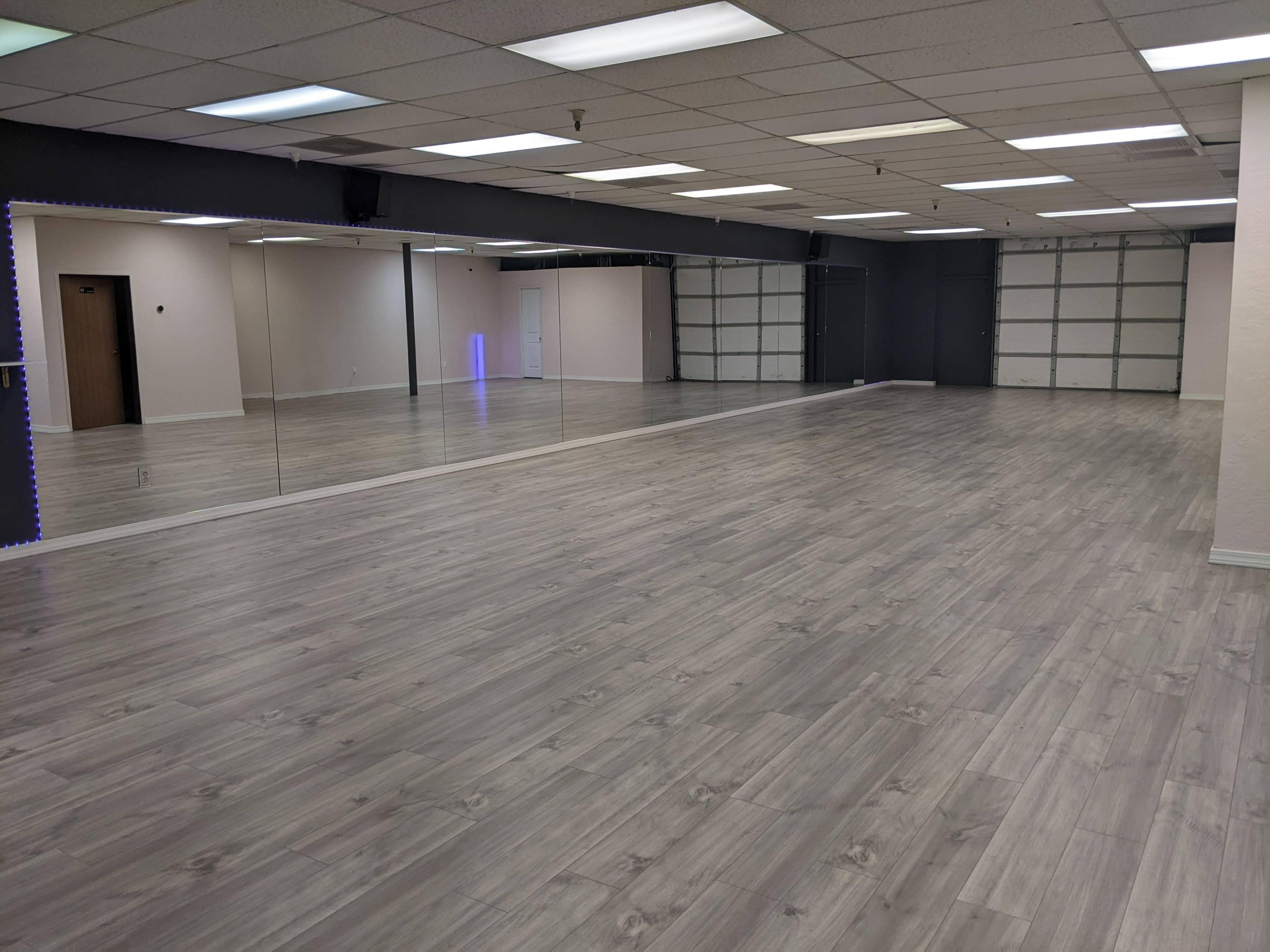 A spacious, empty room with gray wooden flooring and large mirrors on one wall.