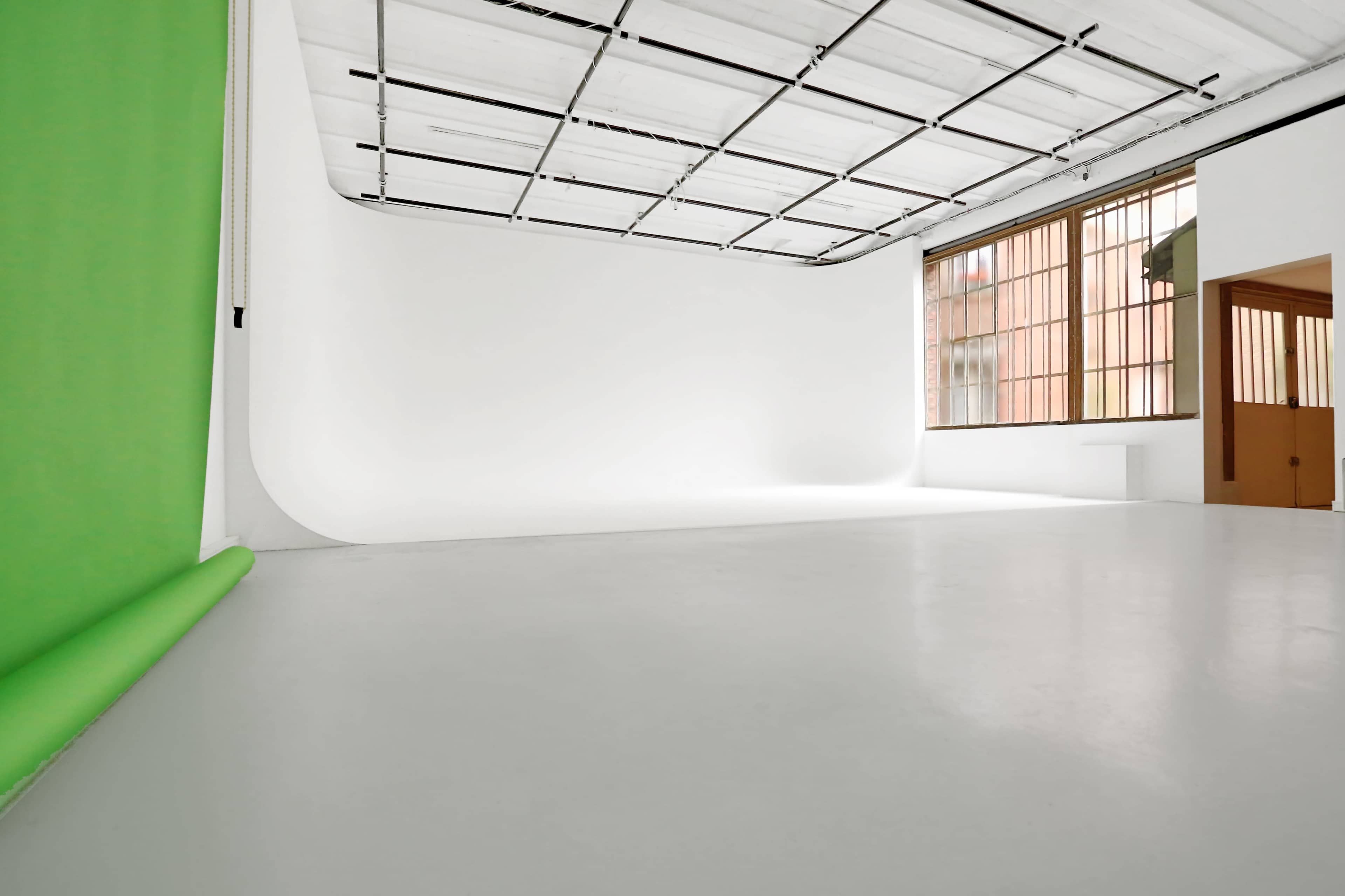 A spacious photography studio with a white background and a green backdrop rolled up on the left.
