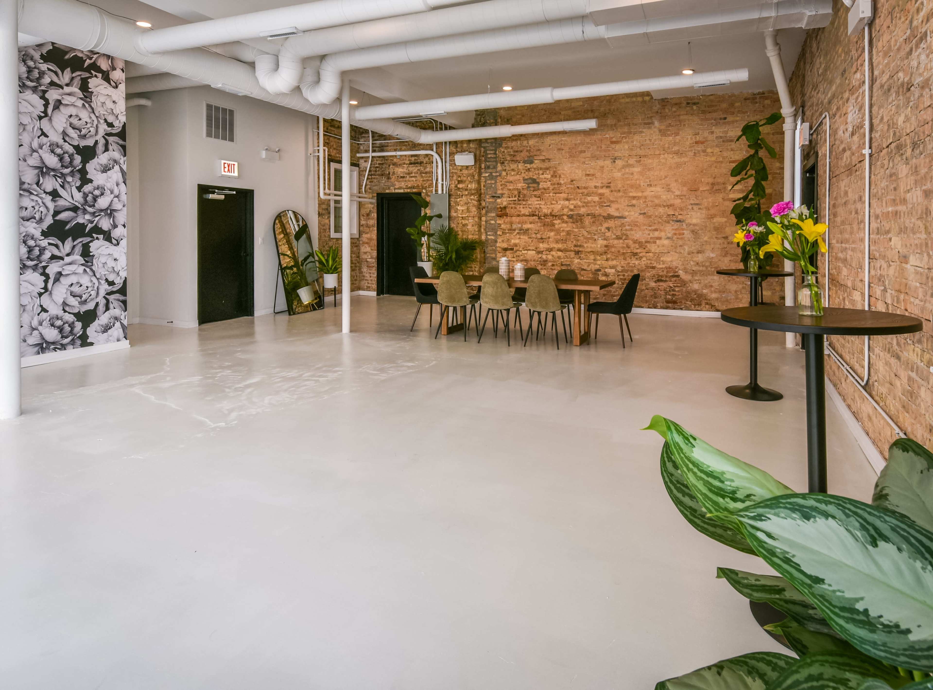 A spacious, modern interior with exposed brick walls, a large table set for dining, and decorative plants.