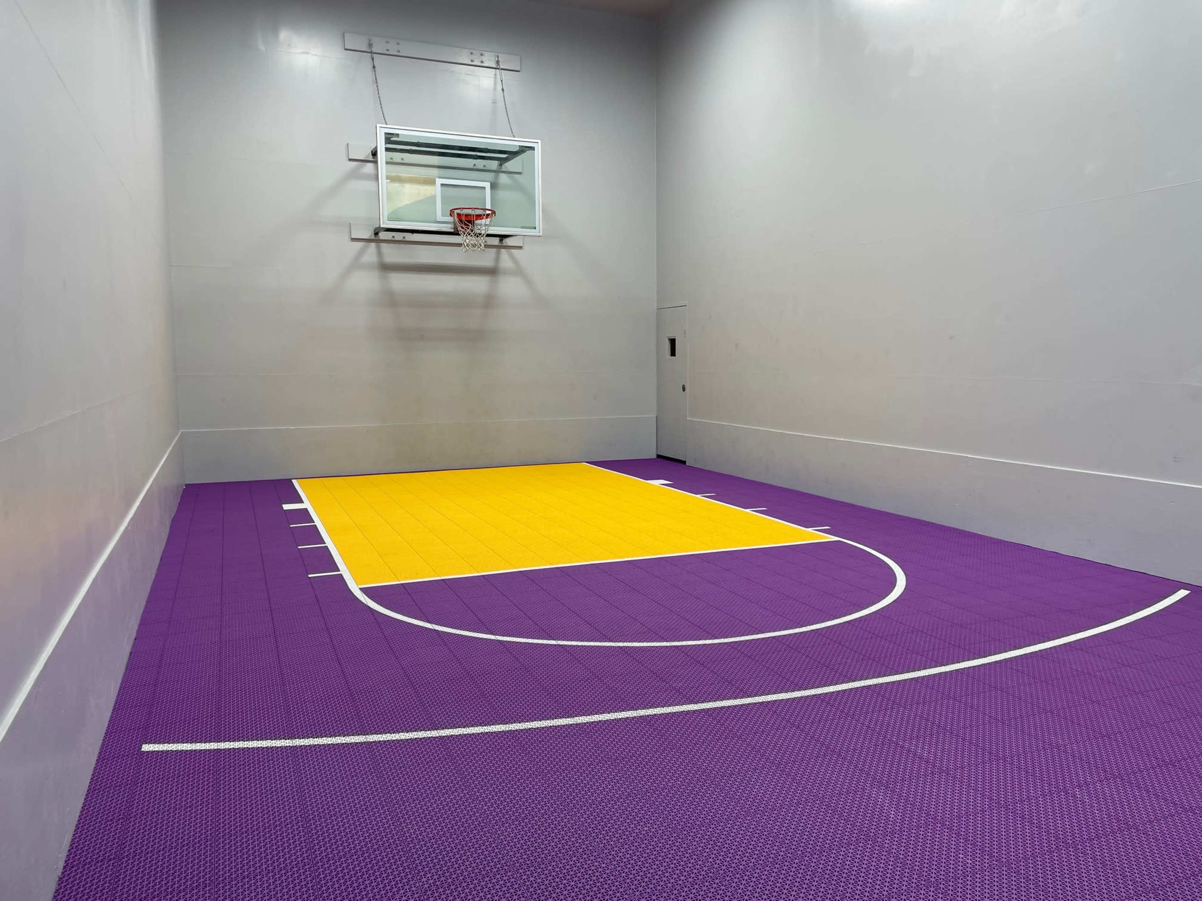 A small indoor basketball court with a yellow and purple floor and a basketball hoop mounted on a gray wall.