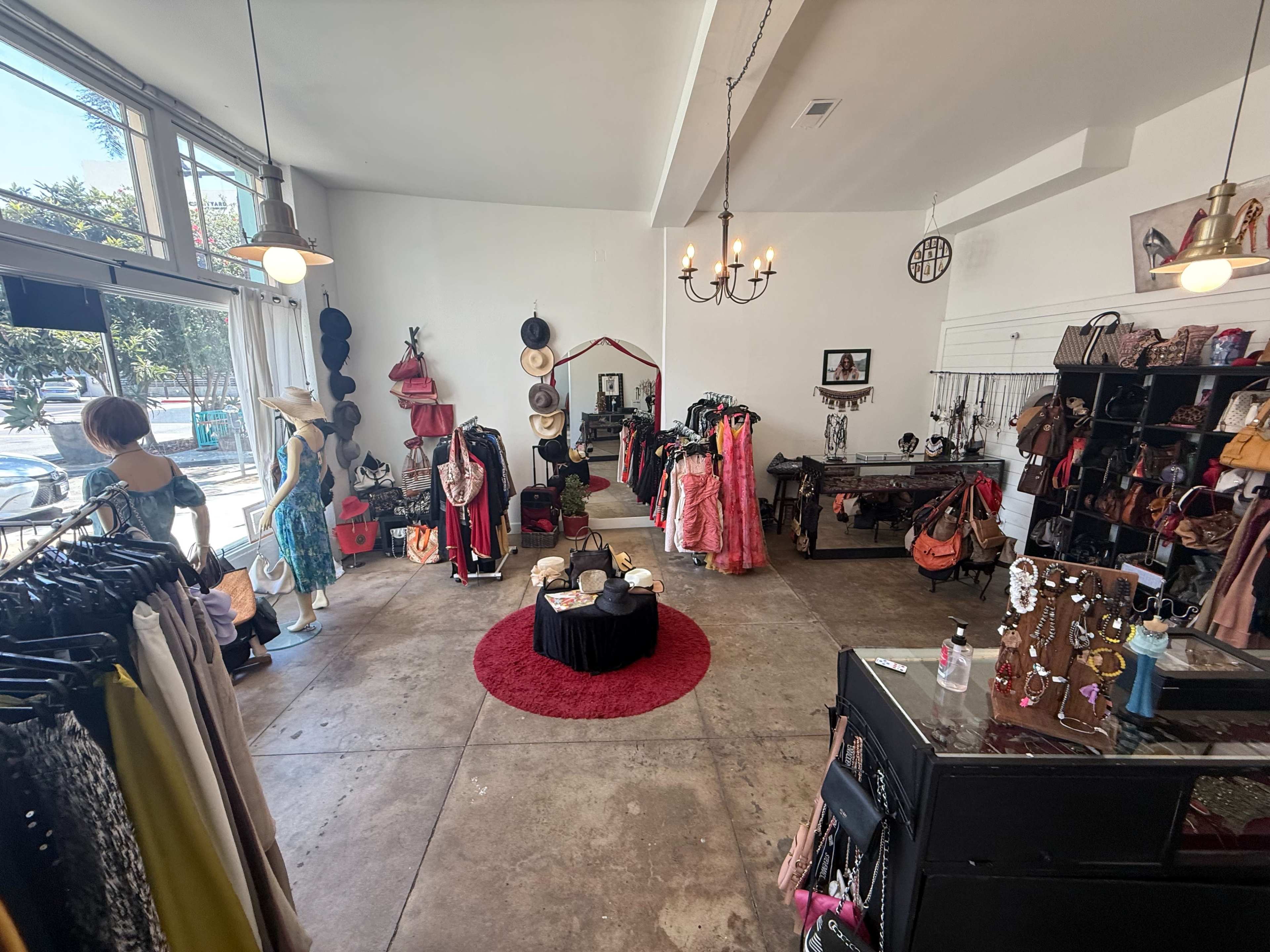 The image shows a boutique interior with clothing, hats, and accessories displayed on racks and mannequins in a well-lit space.
