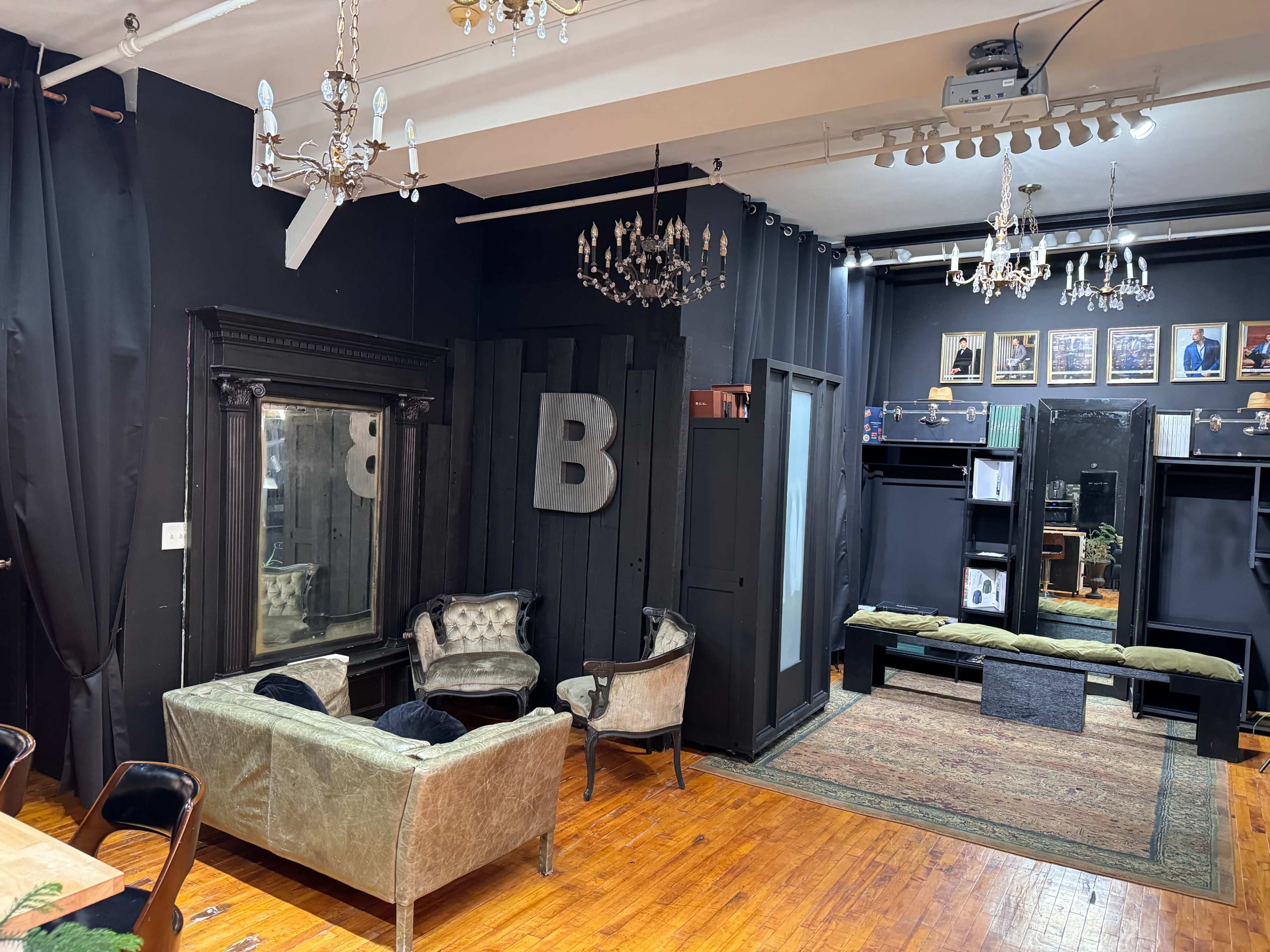 A dark, elegantly furnished room with a vintage sofa, a mirror, and a collection of framed photographs on the wall above a display area.