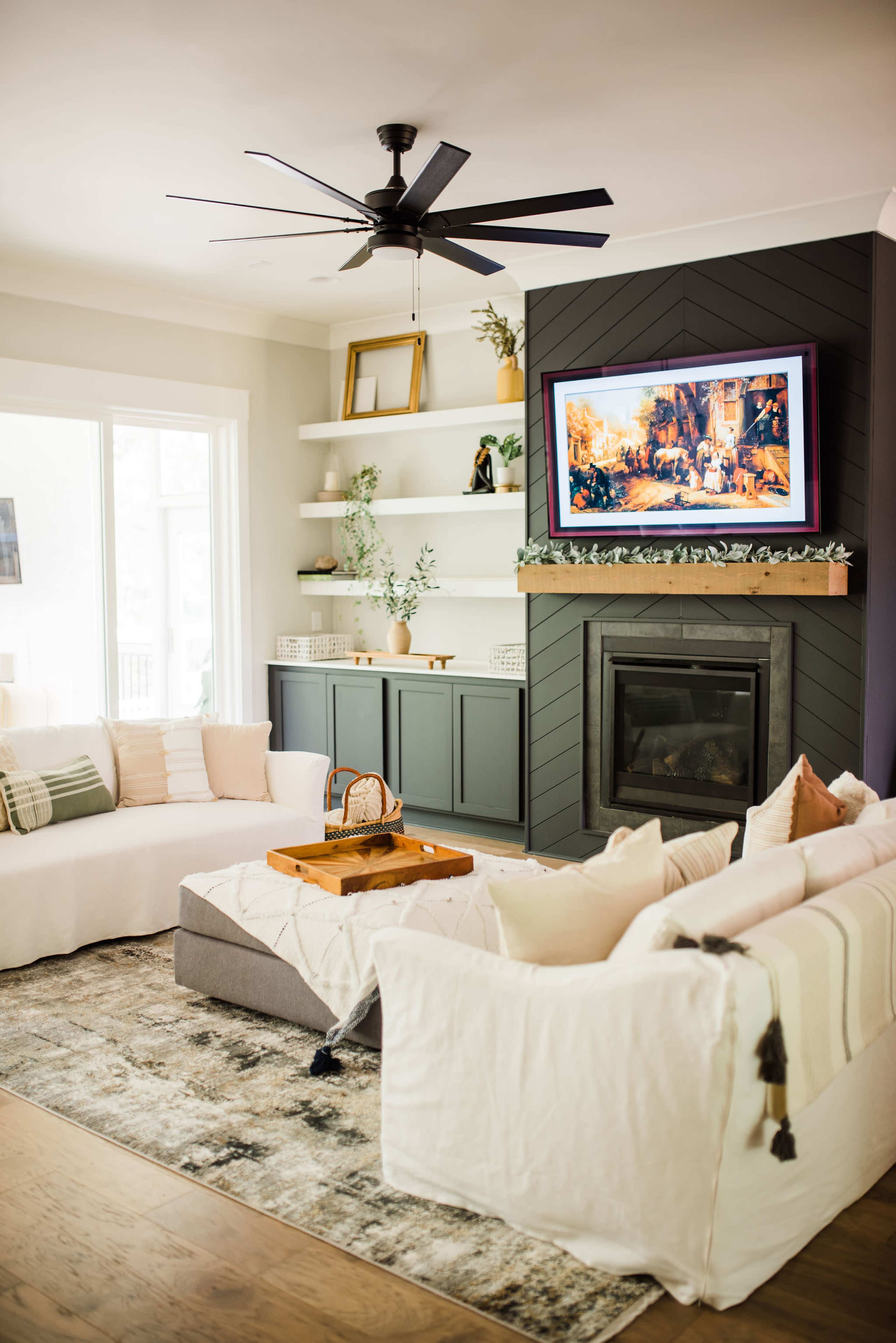 A modern living room features a comfortable seating area, a television mounted above a fireplace, and built-in shelves displaying decorative items.