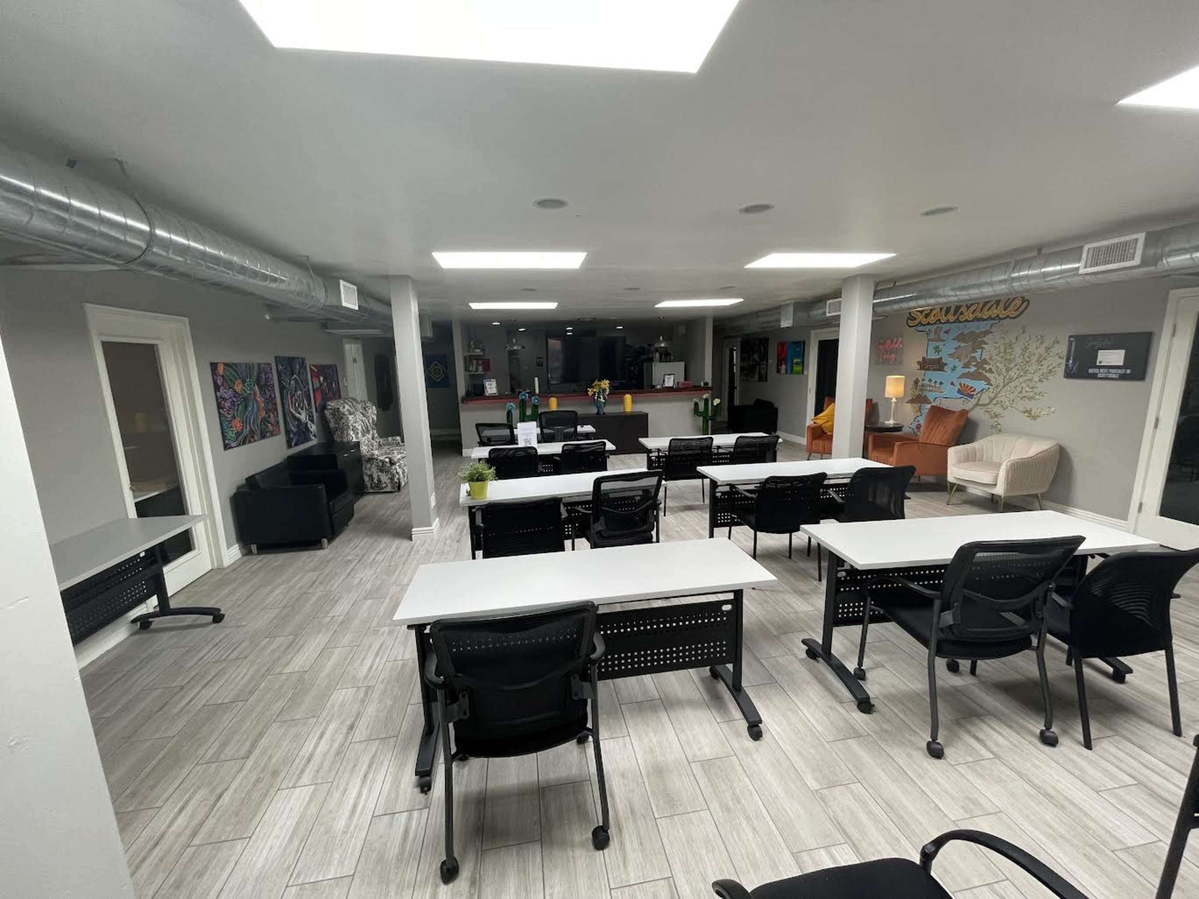 A spacious, modern office environment with multiple desks arranged for work, black chairs, and a lounge area featuring comfortable seating.