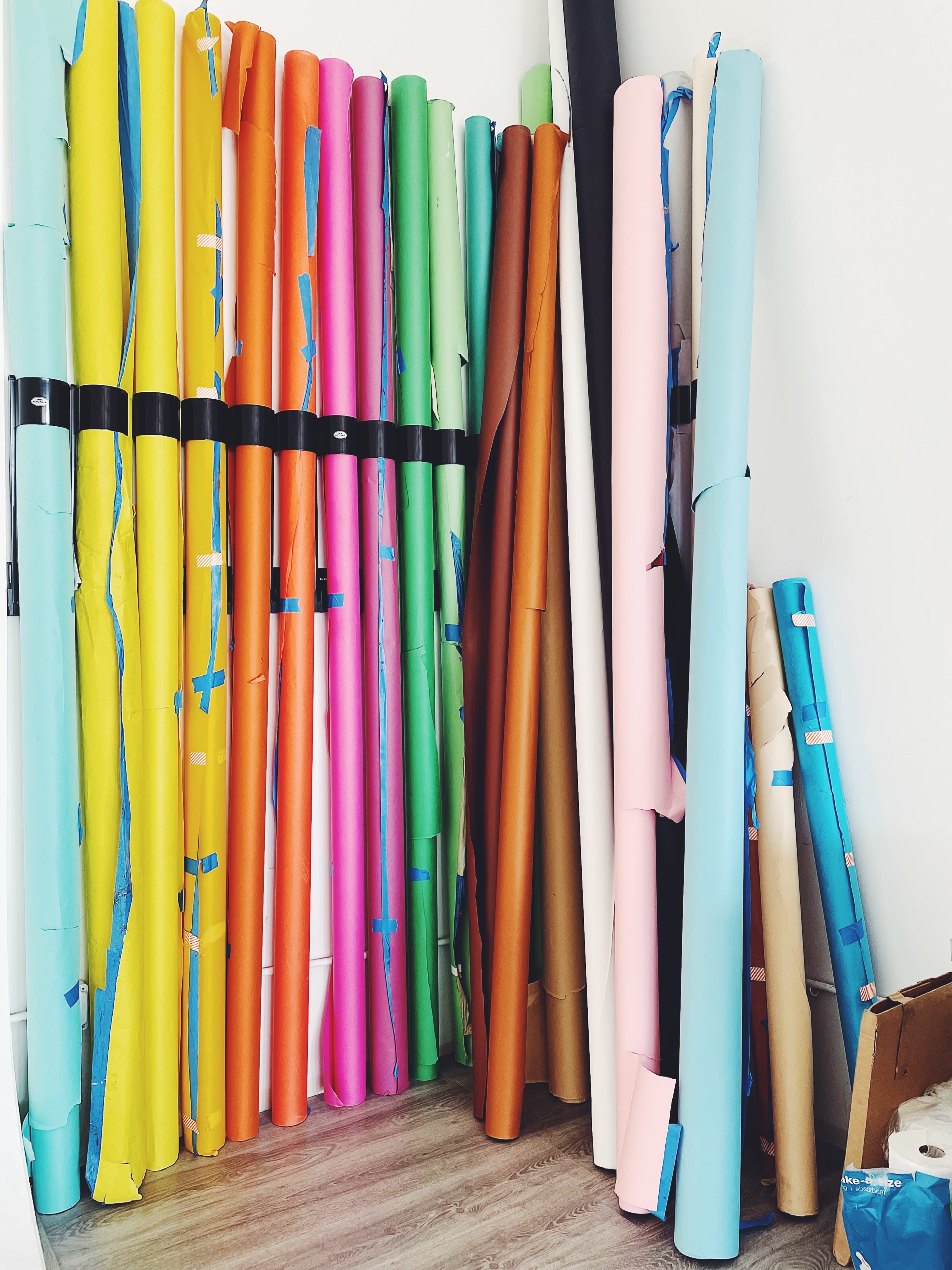 A collection of rolled sheets of colorful paper organized against a wall in a room.