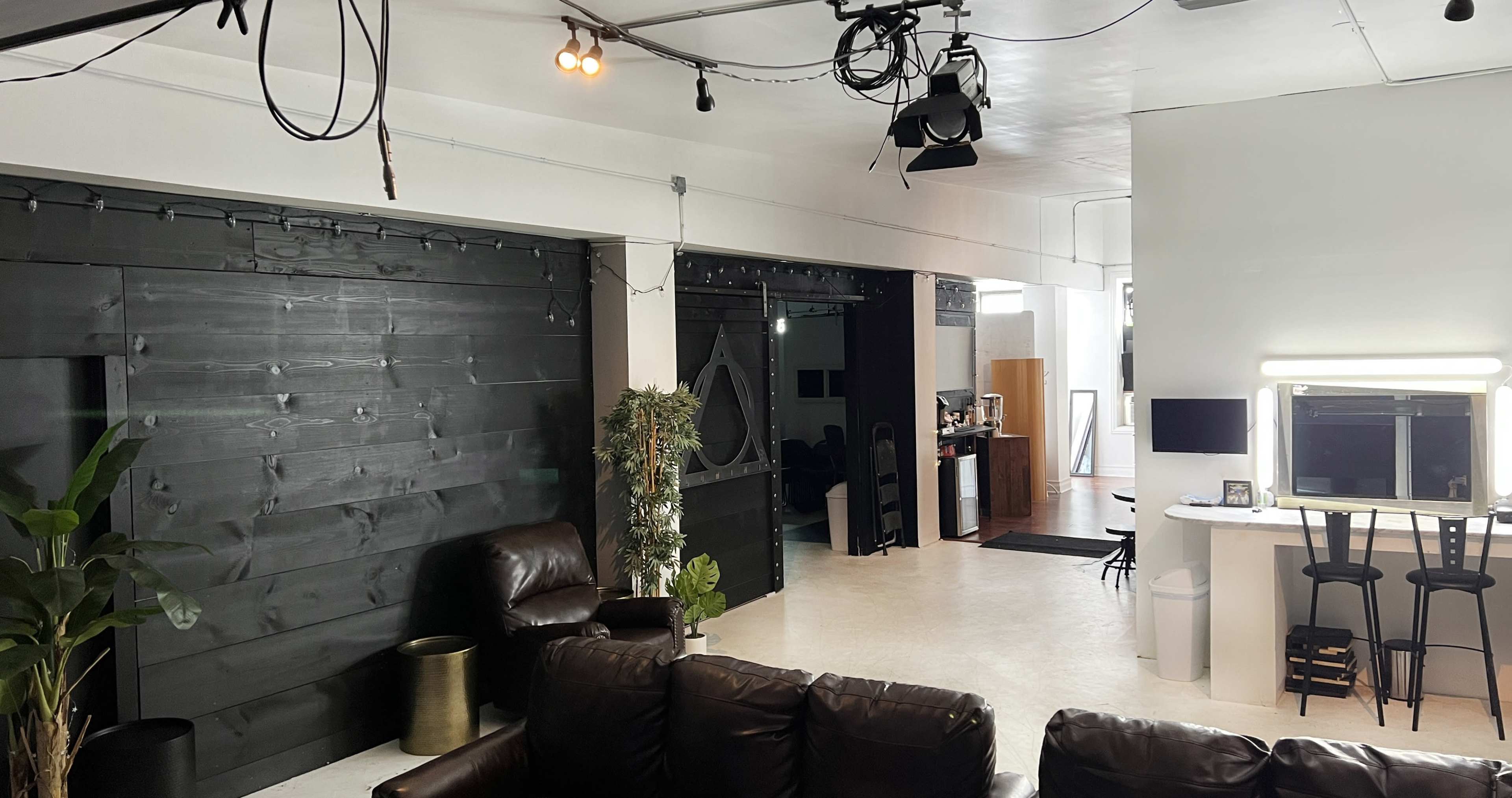 A modern, open space with dark wooden walls, a seating area with brown leather couches, and a bar-like setup with tall stools and lighting.