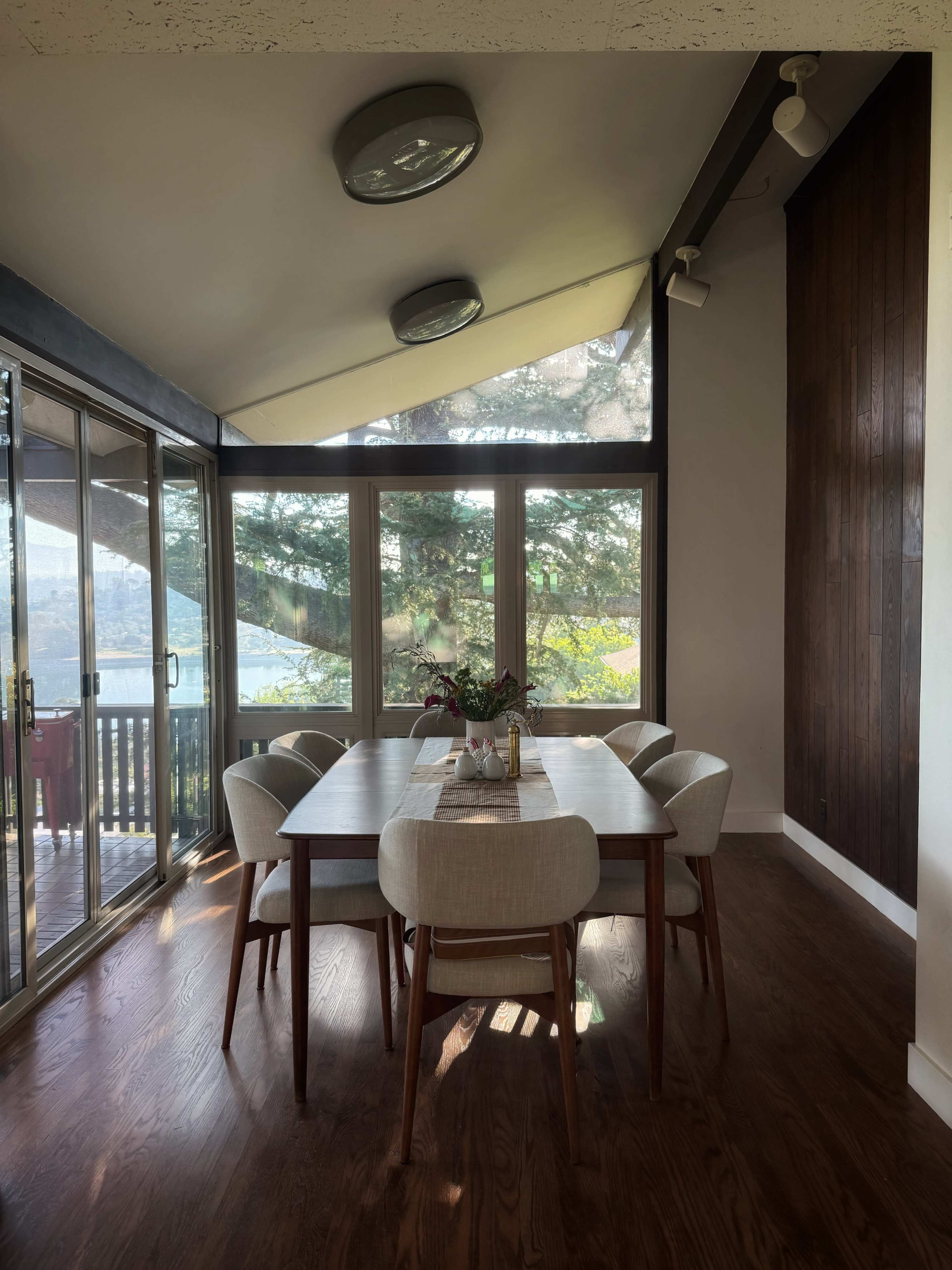 A dining table with six chairs is positioned near large windows that overlook a wooded area.