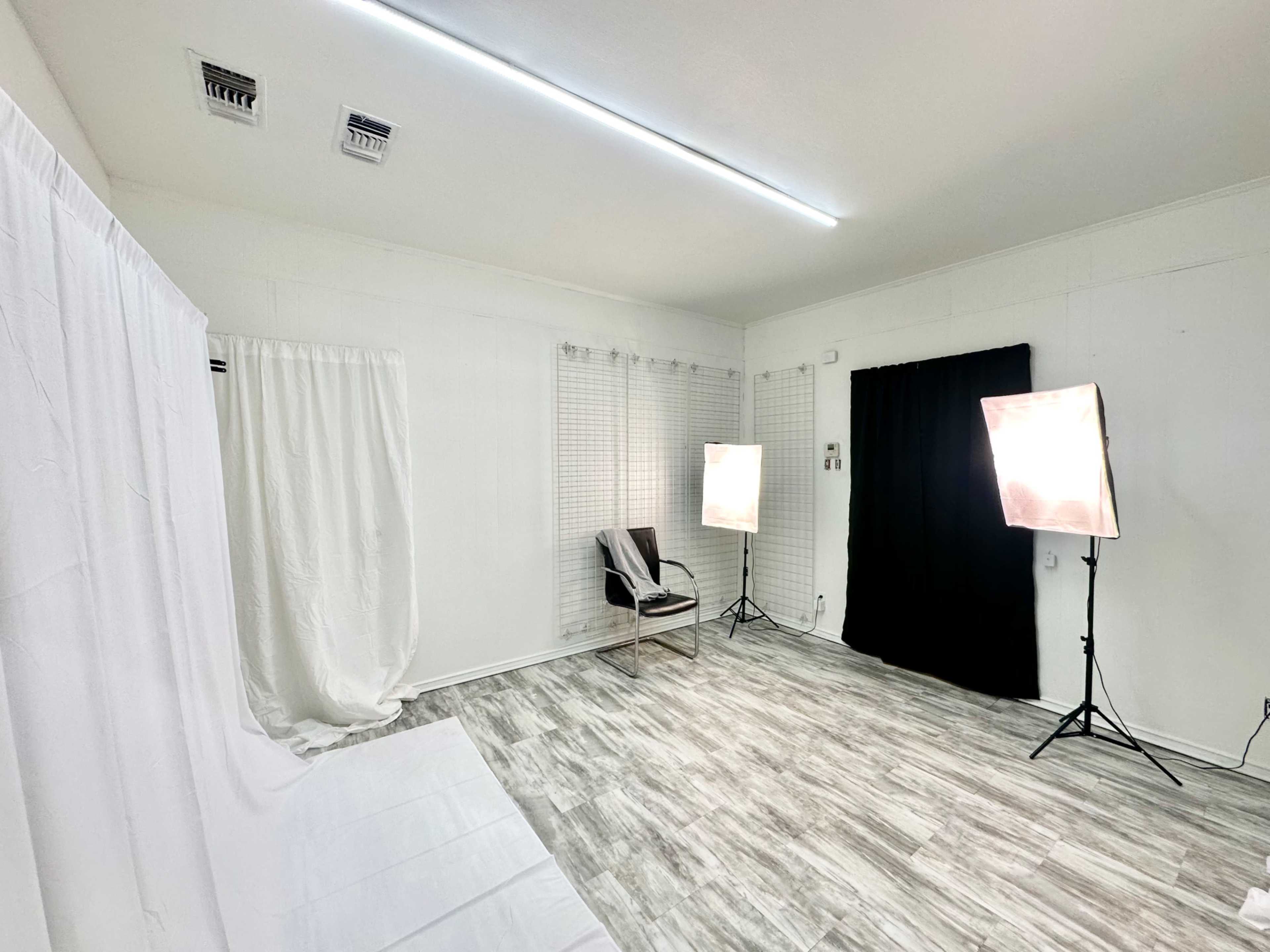 A bright studio space with a white backdrop, a black curtain, and two softbox lights positioned on either side.