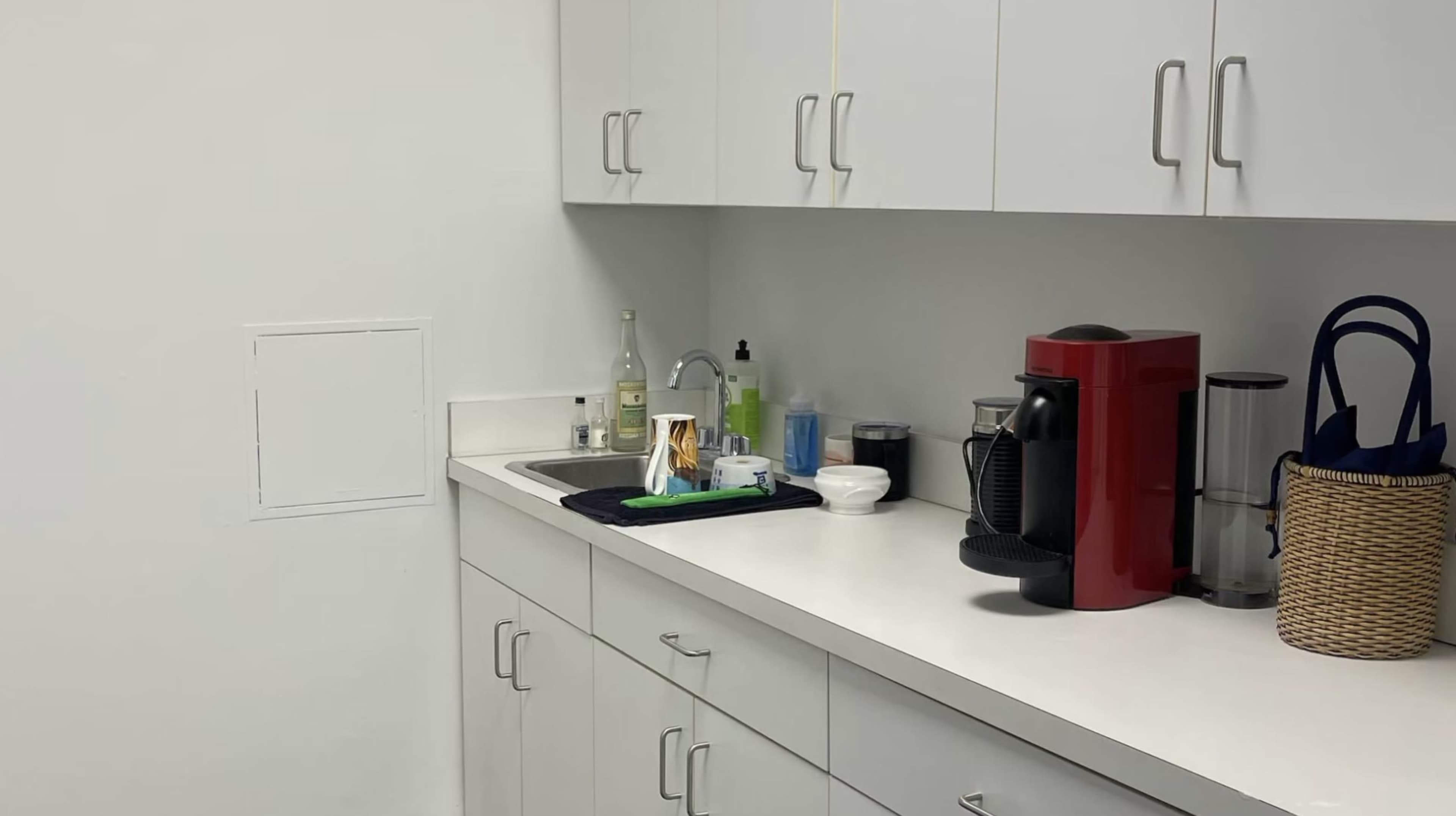 A clean kitchen countertop features a red coffee maker, various utensils, and bottles in a well-organized setting.
