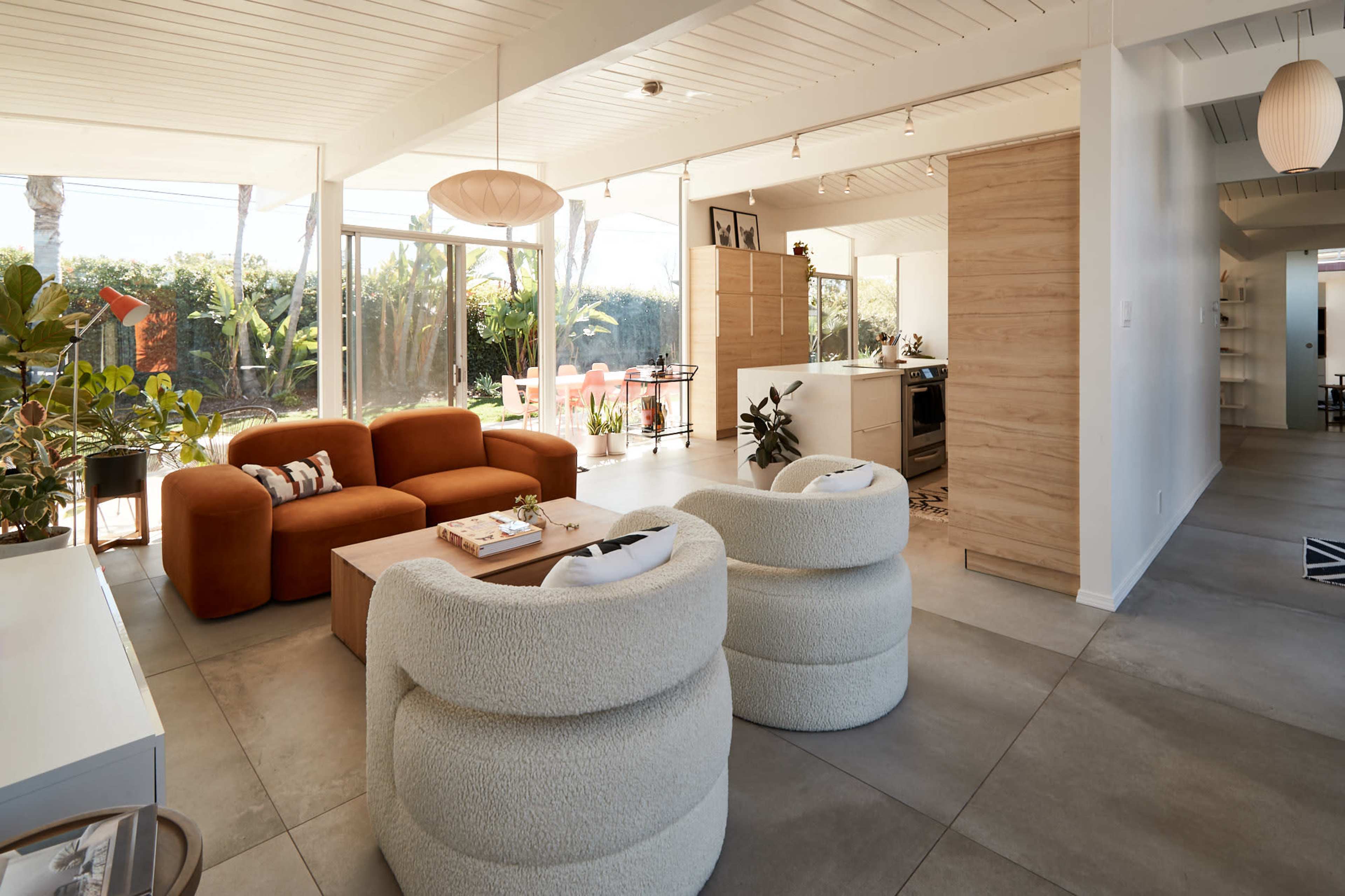 A modern living space with a brown sofa, two round white chairs, and a kitchen area visible in the background.