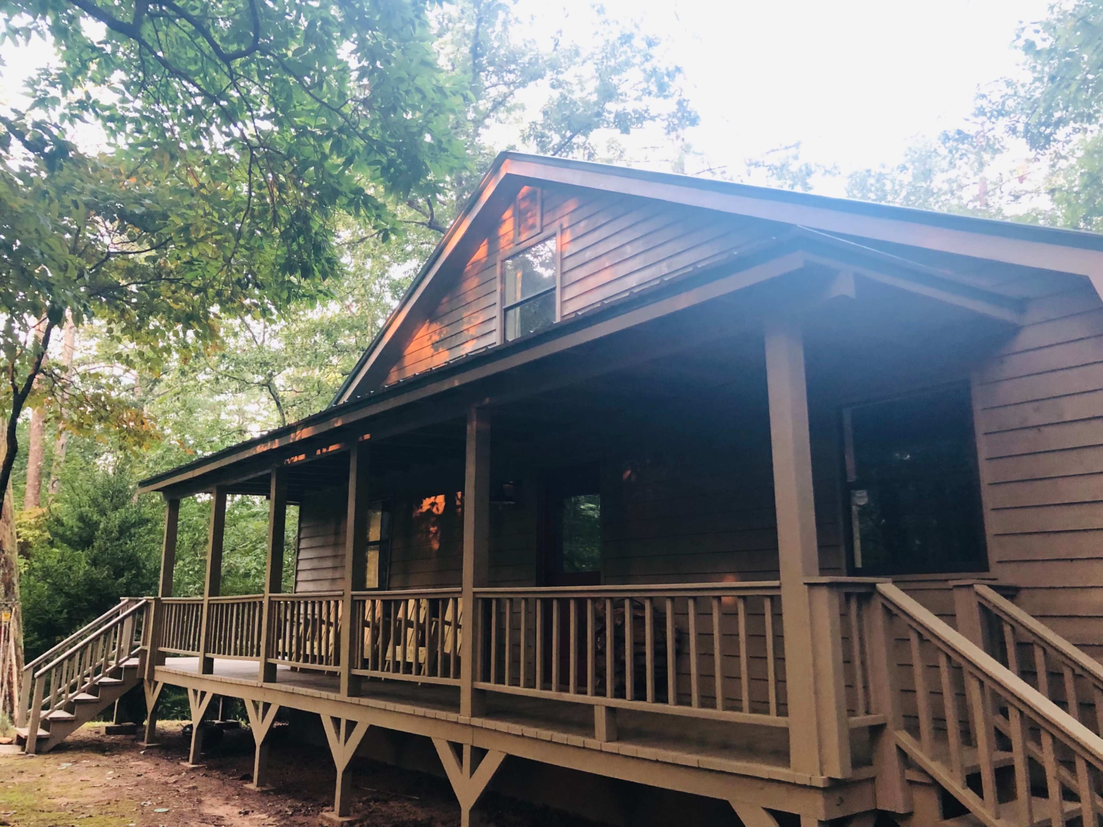 A wooden house with a front porch sits among trees in a wooded area.
