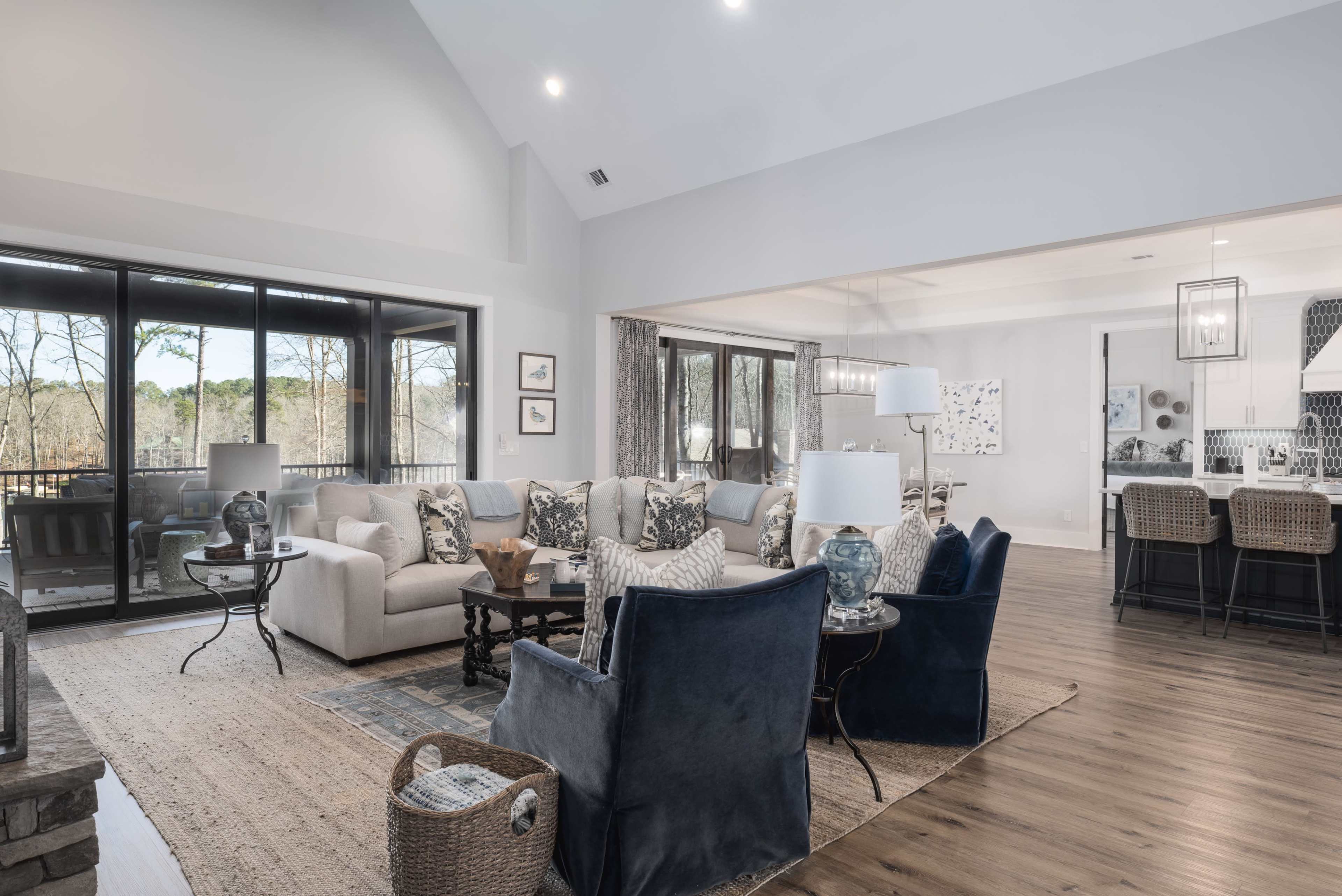 The spacious living area features a large sectional sofa, two blue armchairs, and a dining area visible in the background, all illuminated by natural light from large windows.