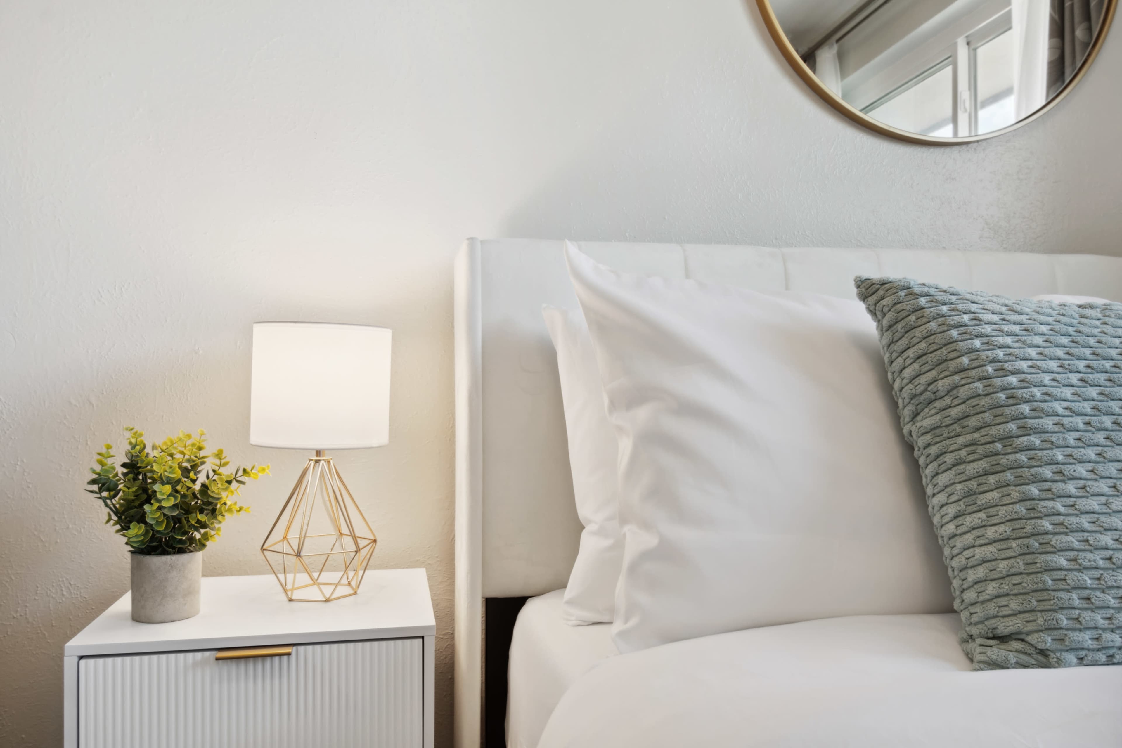 A neatly made bed with a decorative pillow and a bedside table featuring a geometric lamp and a small plant.