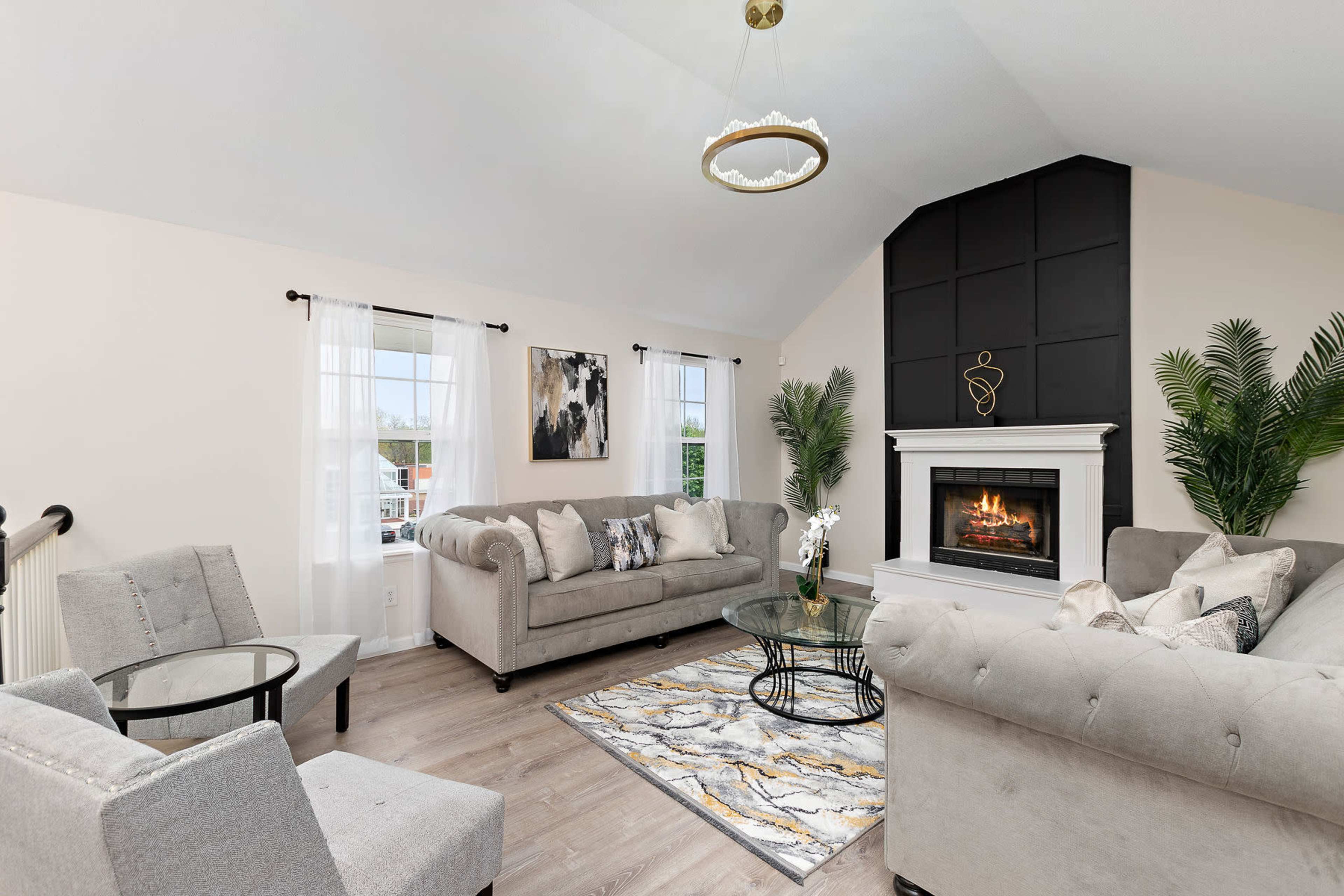 A cozy living room features a fireplace, a gray sectional sofa, and large windows with sheer curtains.