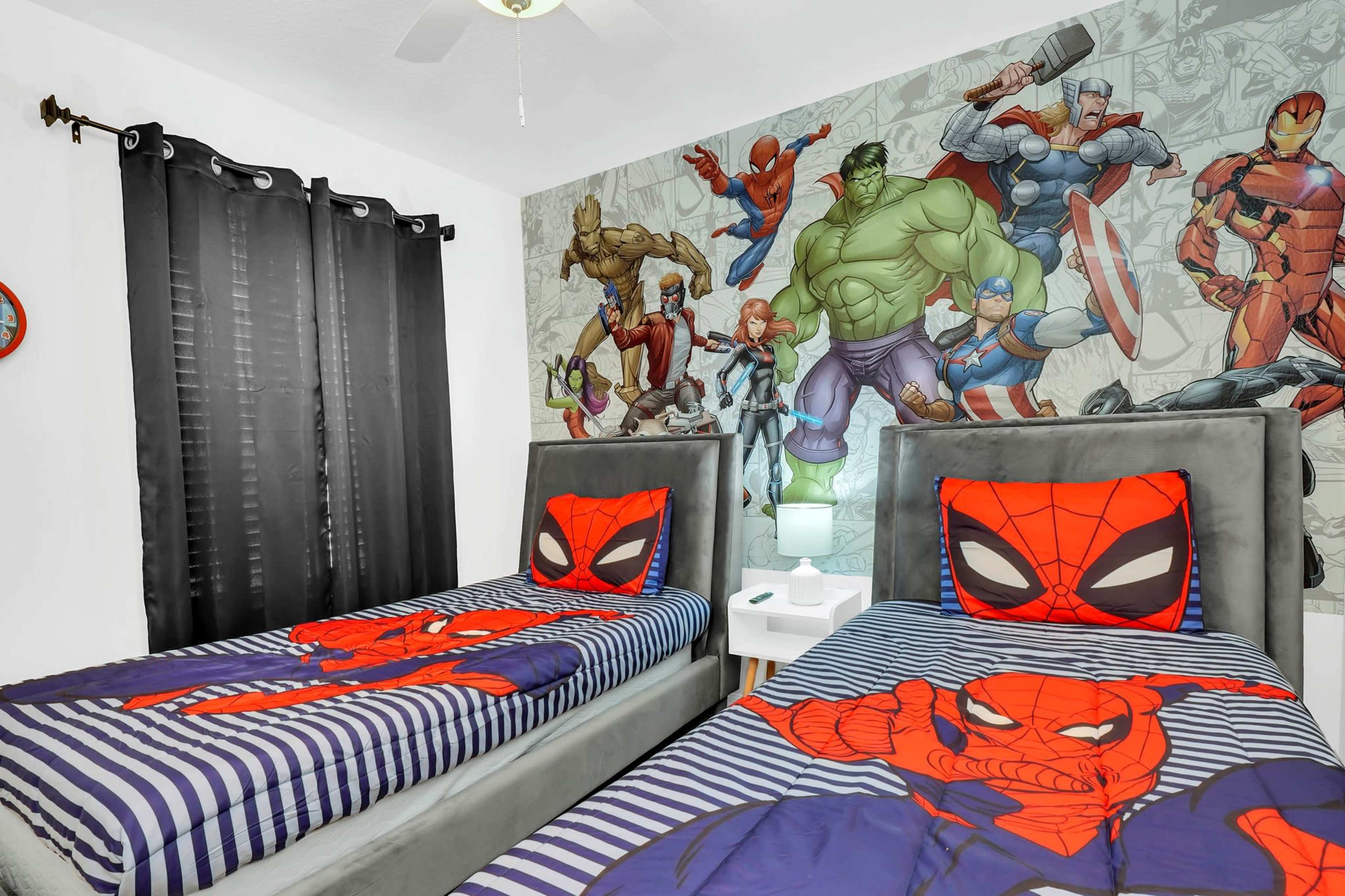 A bedroom with two twin beds featuring Spider-Man-themed bedding and a wall mural of various superhero characters.