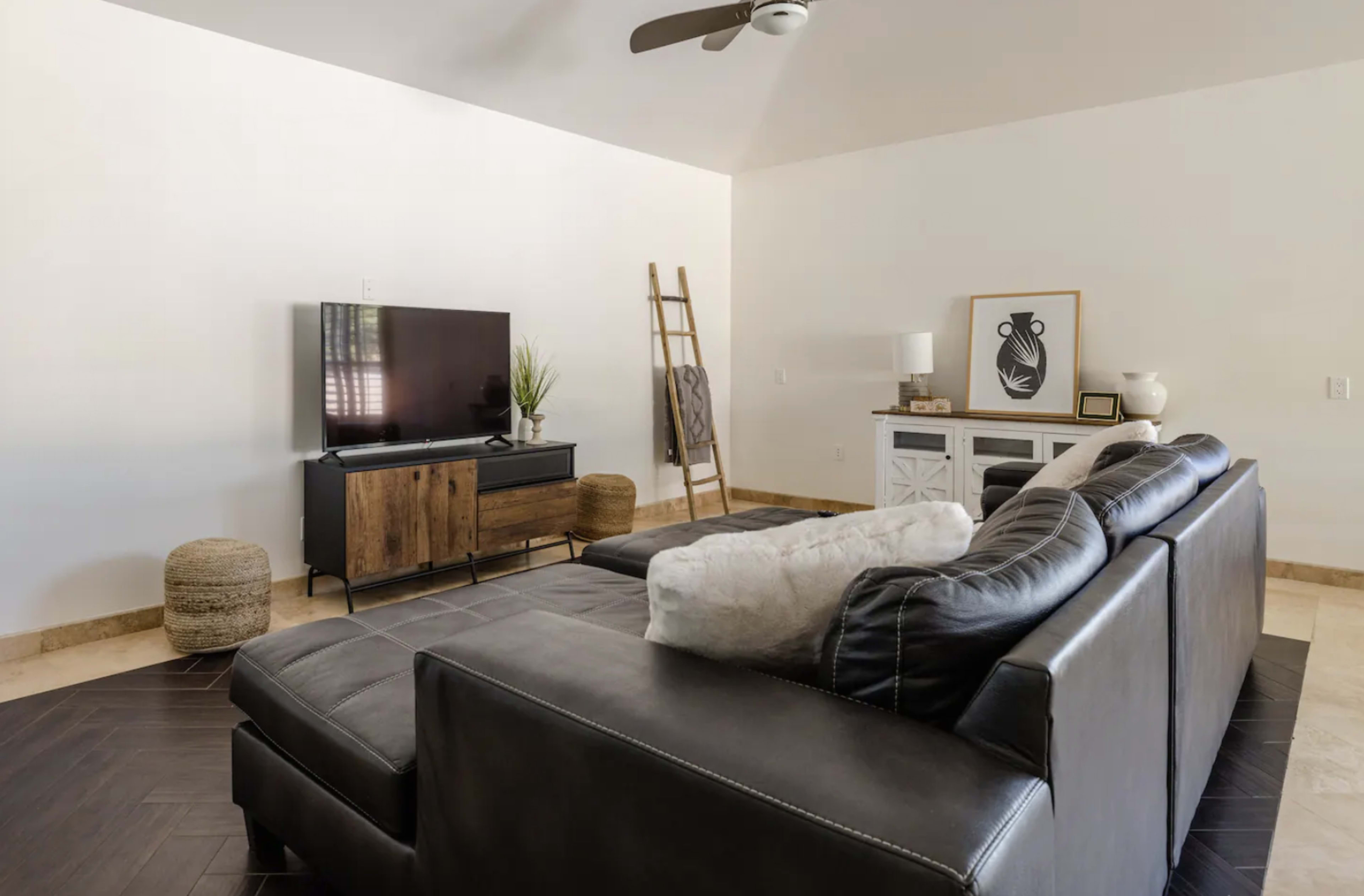 A modern living room with a black sectional sofa, a television on a wooden stand, and a decorative ladder against the wall.