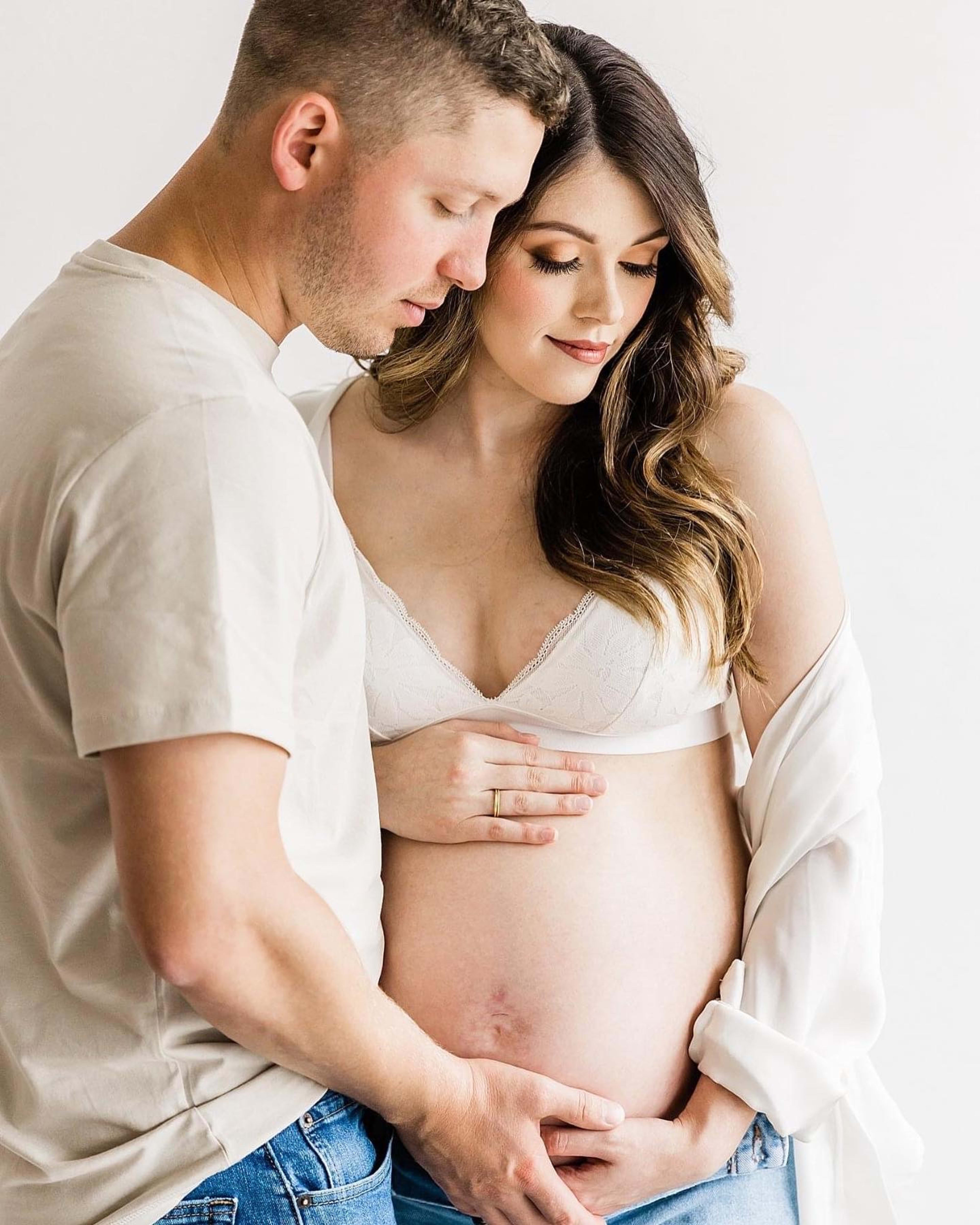 Un shooting photo de maternité d’un couple devant un fond blanc.