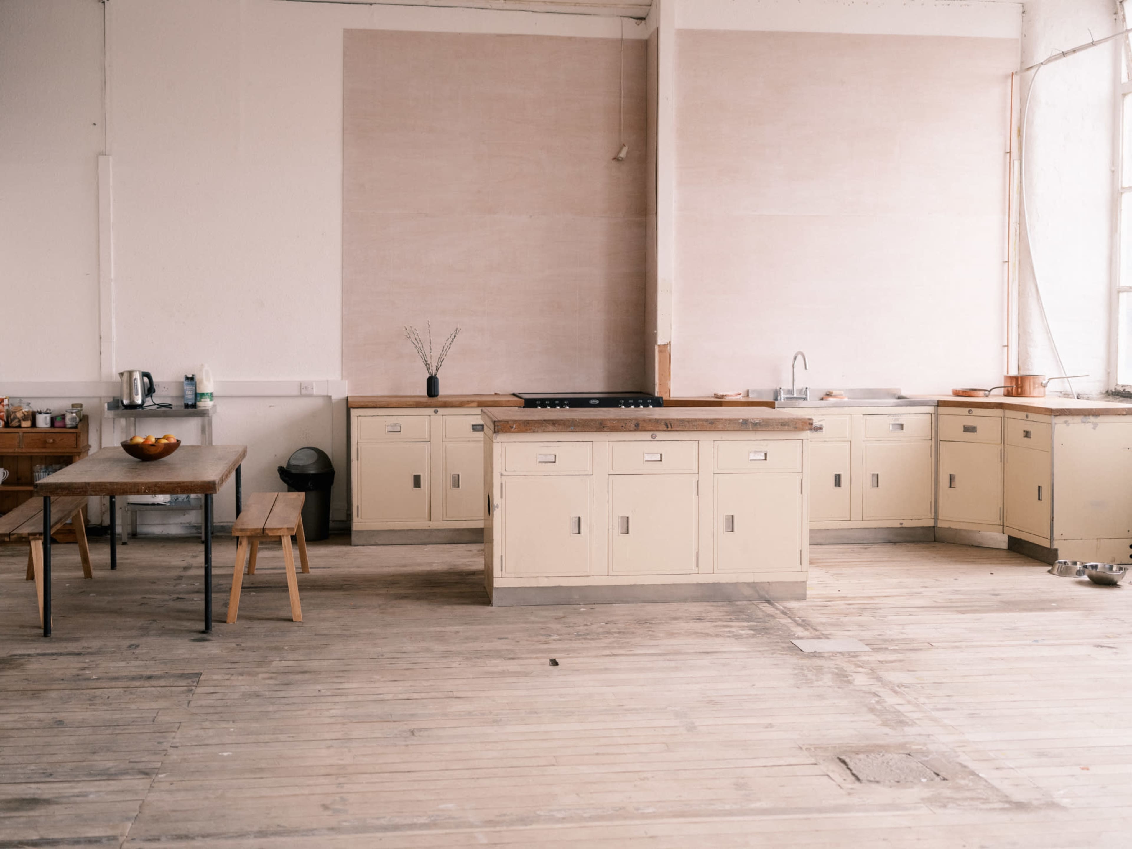 The image shows a spacious kitchen with a central island, wooden countertops, and a dining table against a wall.