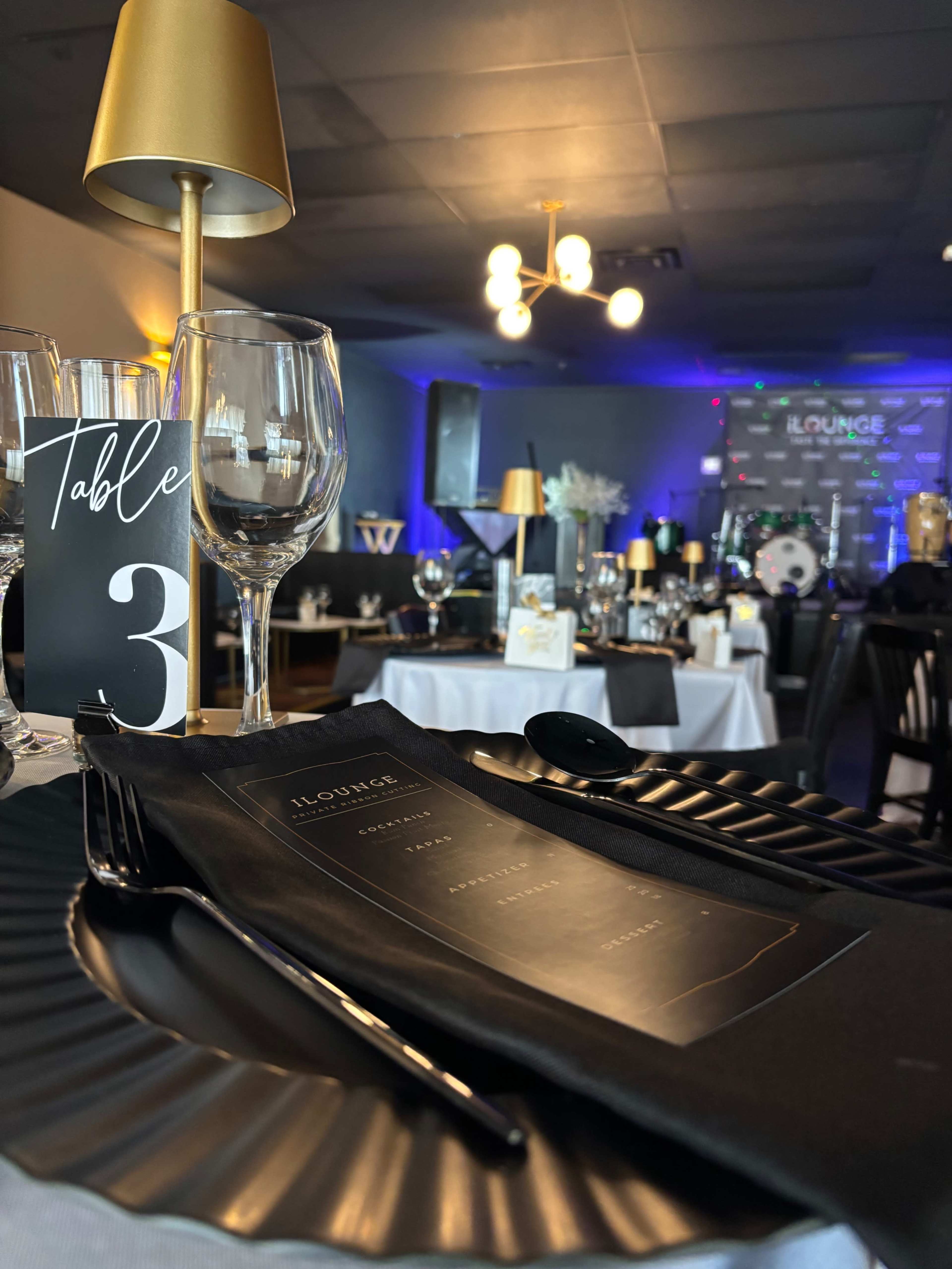 A table setting is arranged with elegant black menus, glassware, and decorative elements in a beautifully lit lounge area.