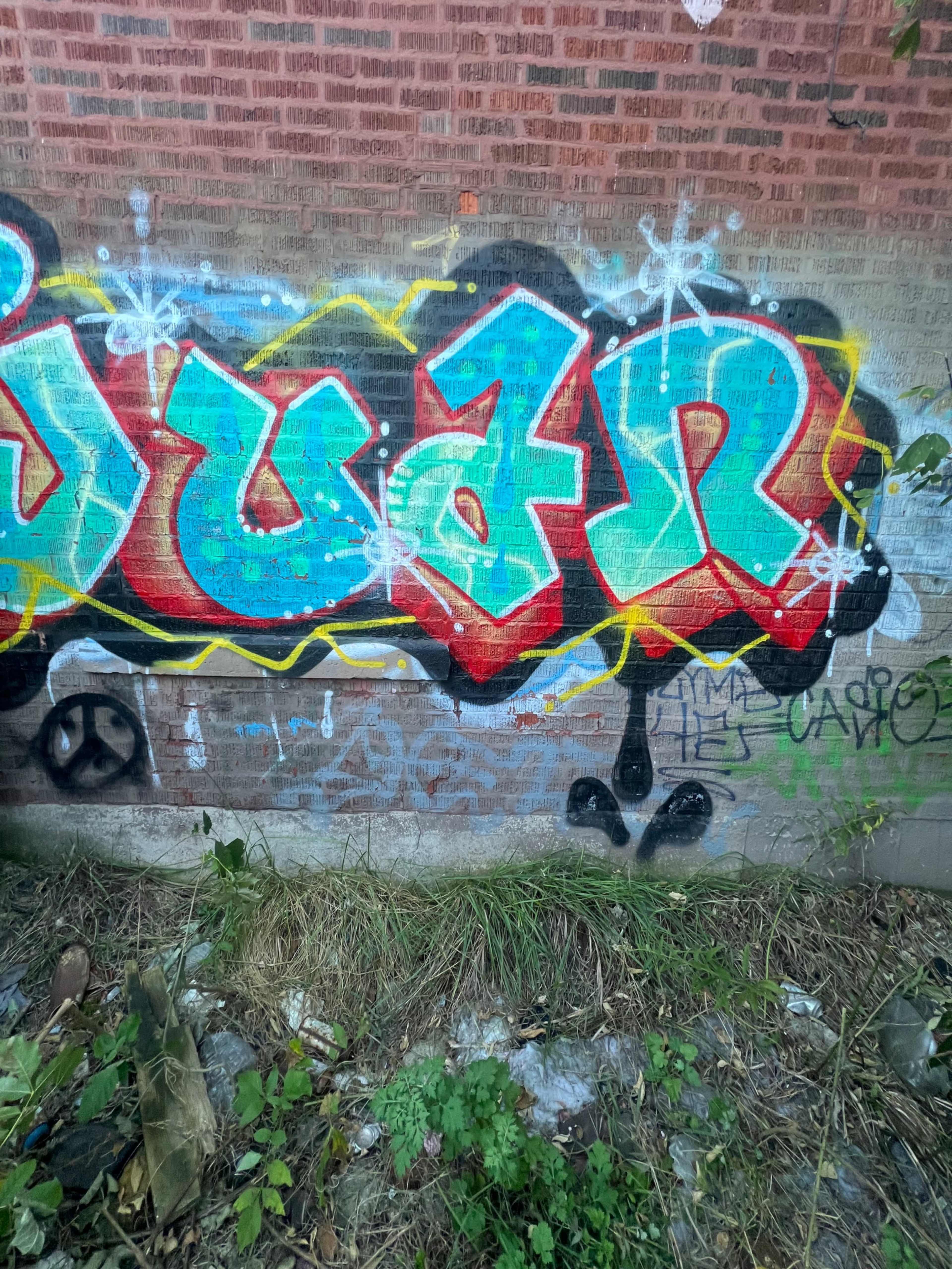 The image shows a colorful graffiti mural on a brick wall featuring the name "Juan" in prominent letters, surrounded by various tags and symbols.