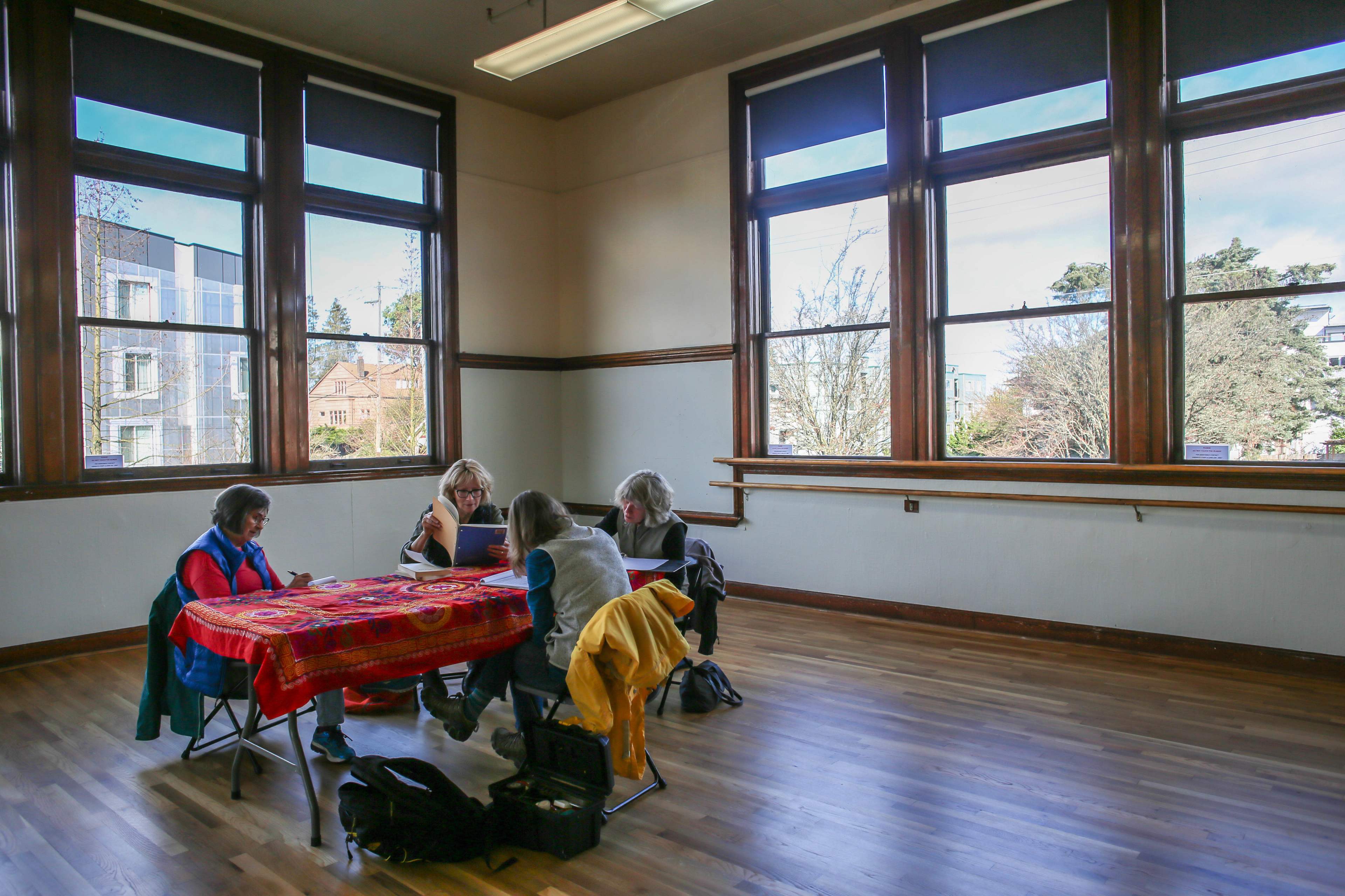 Four people sit around a red table in a spacious room with large windows.