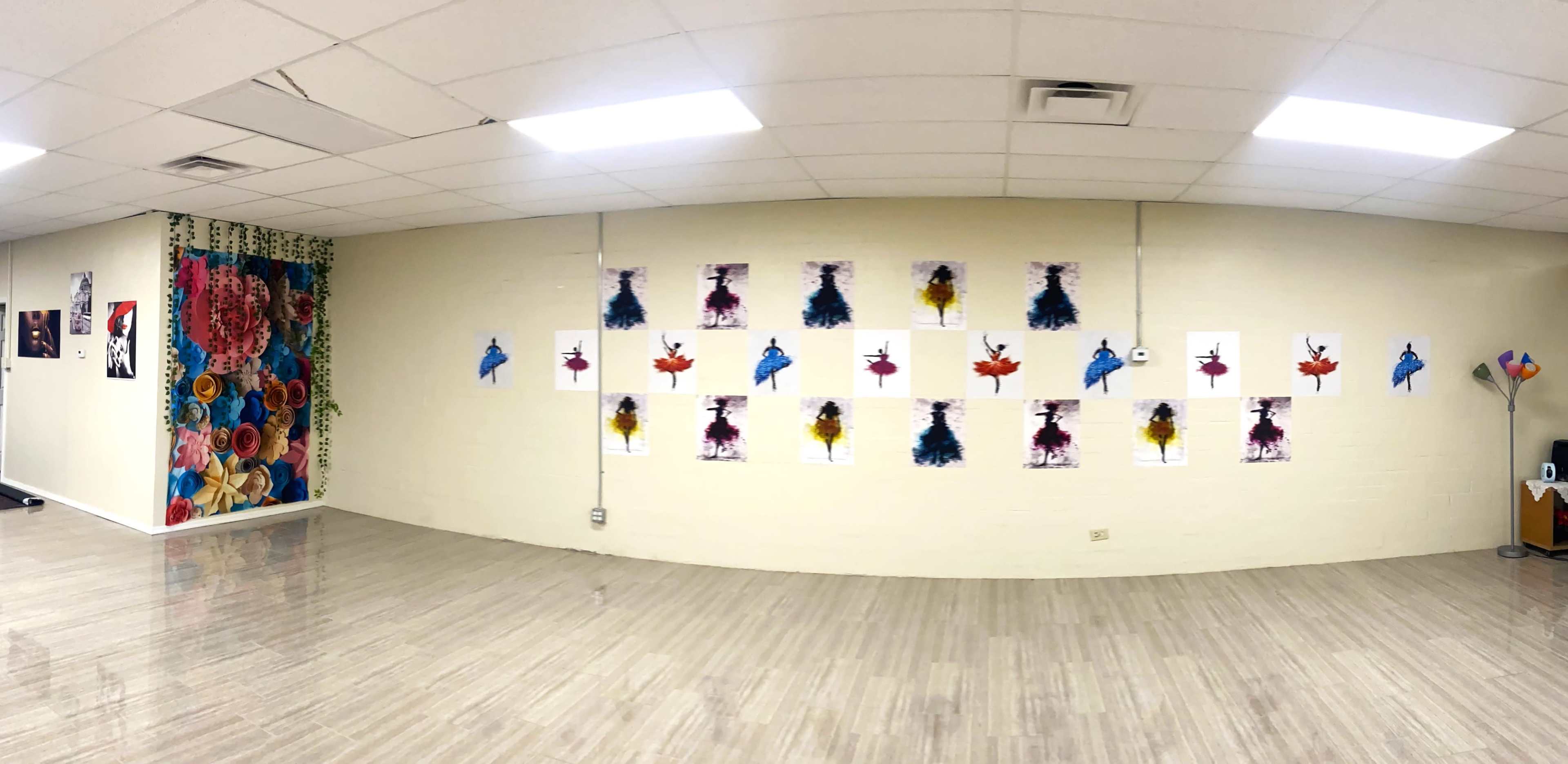 A spacious room with a light-colored wall decorated with multiple art prints of colorful birds and abstract designs, alongside a wall featuring a vibrant floral mural.