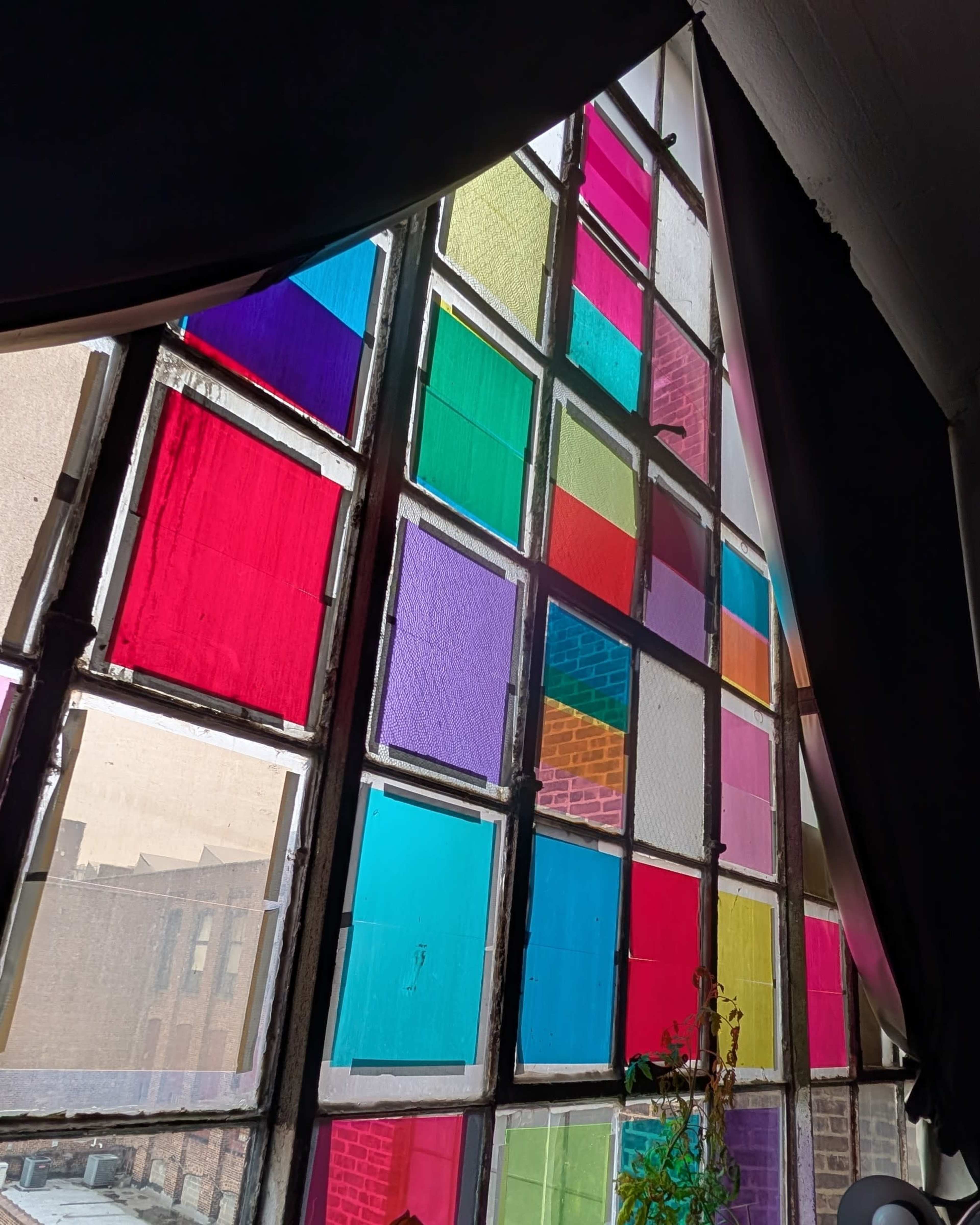 The image shows a large window made up of colorful stained glass panes in a grid pattern, filtering light into the interior space.