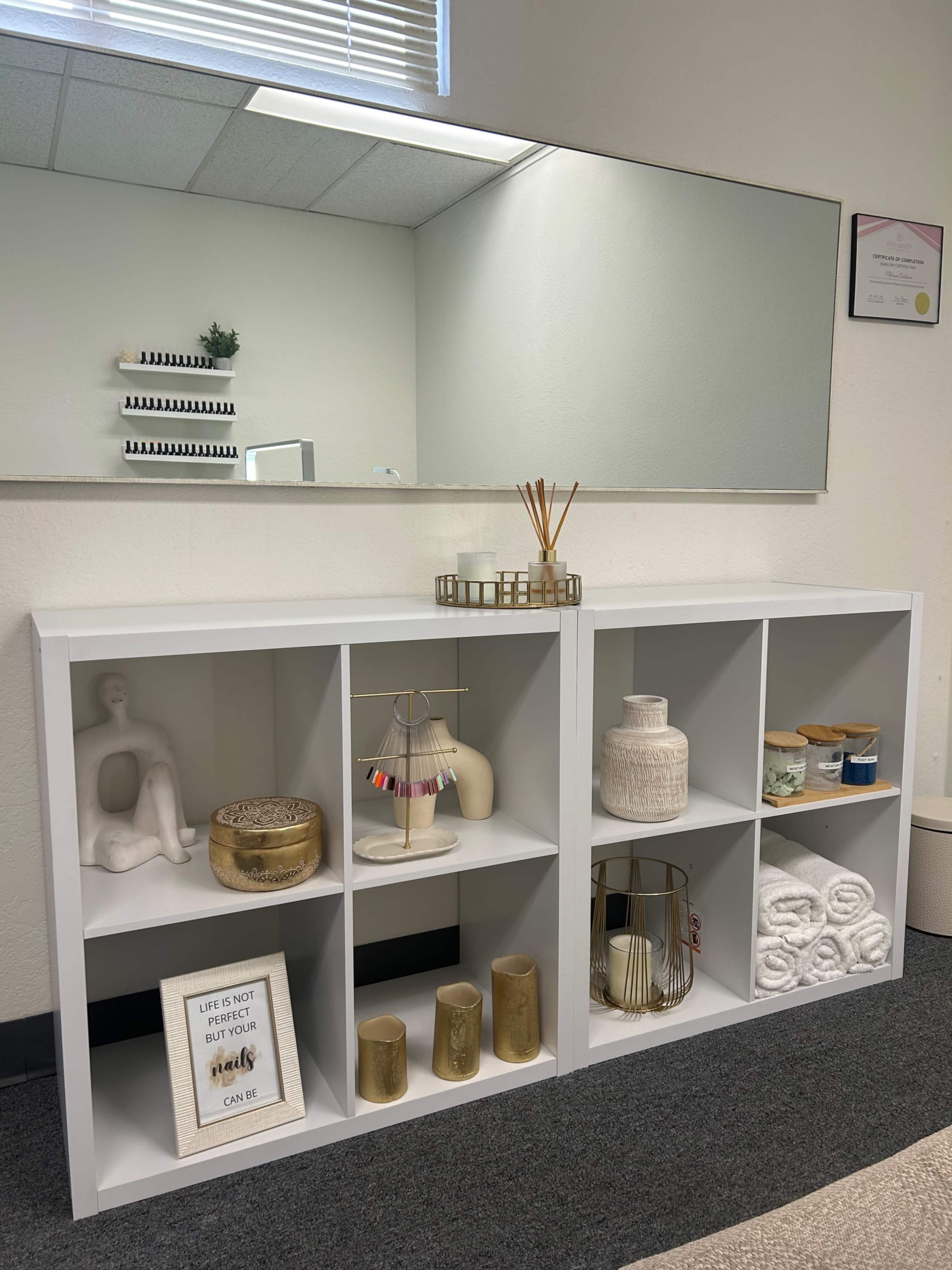 A white shelving unit with decorative items and towels is positioned against a wall, reflecting a mirror above it.