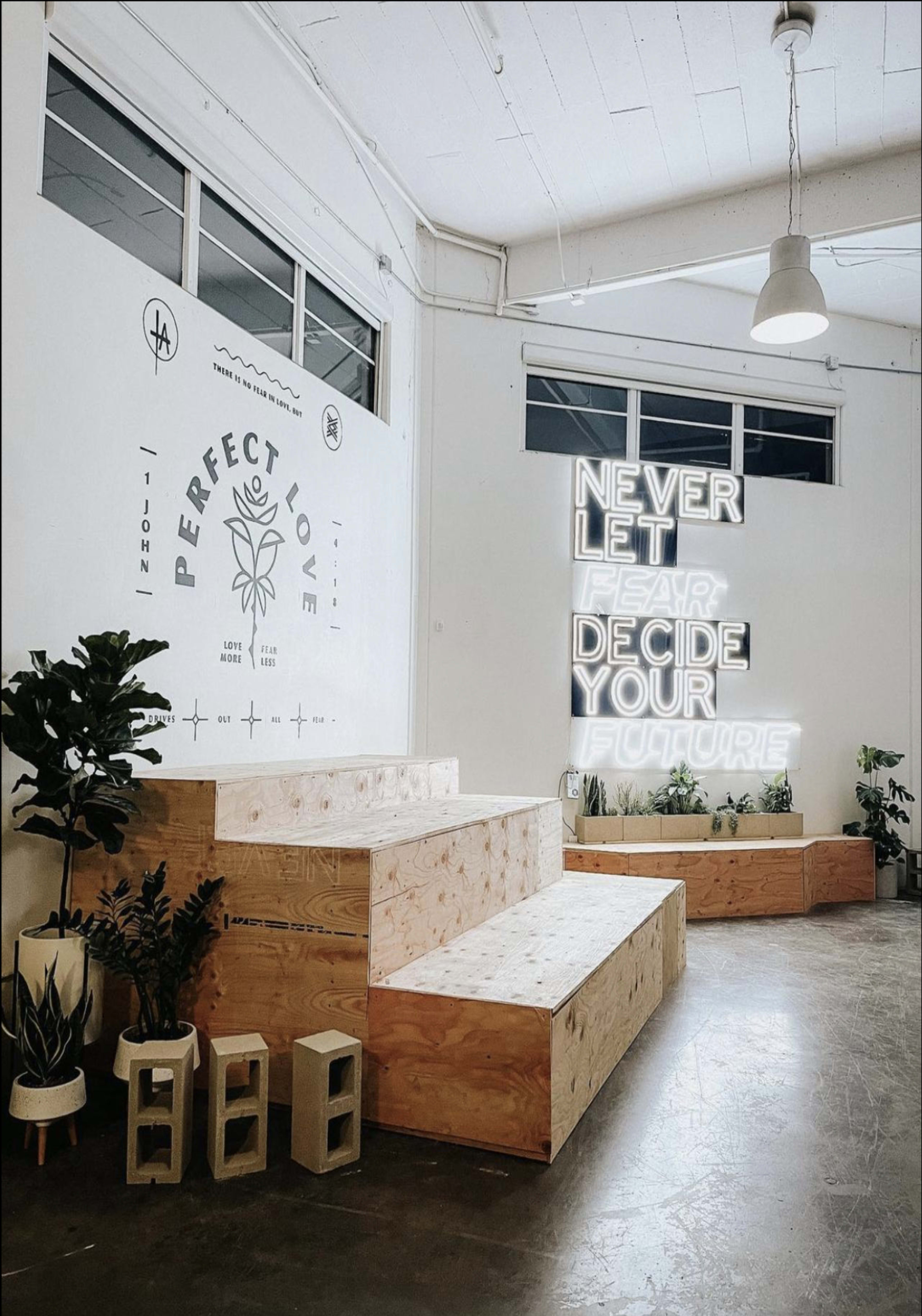 A modern interior space featuring wooden steps, potted plants, and neon signage that reads "NEVER LET FEAR DECIDE YOUR FUTURE."