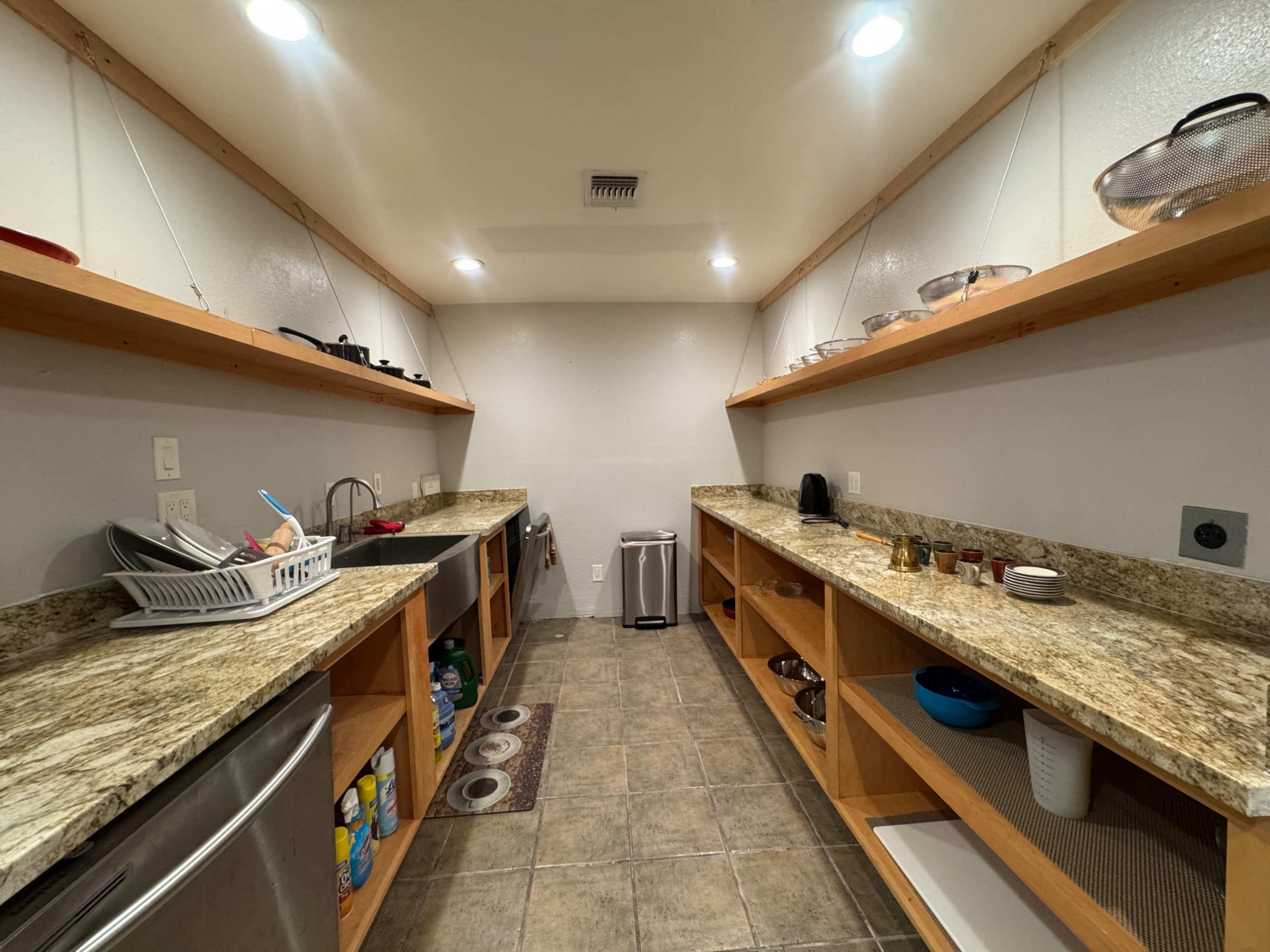 The image shows a bright kitchen with wooden shelves, granite countertops, and organized appliances on either side.