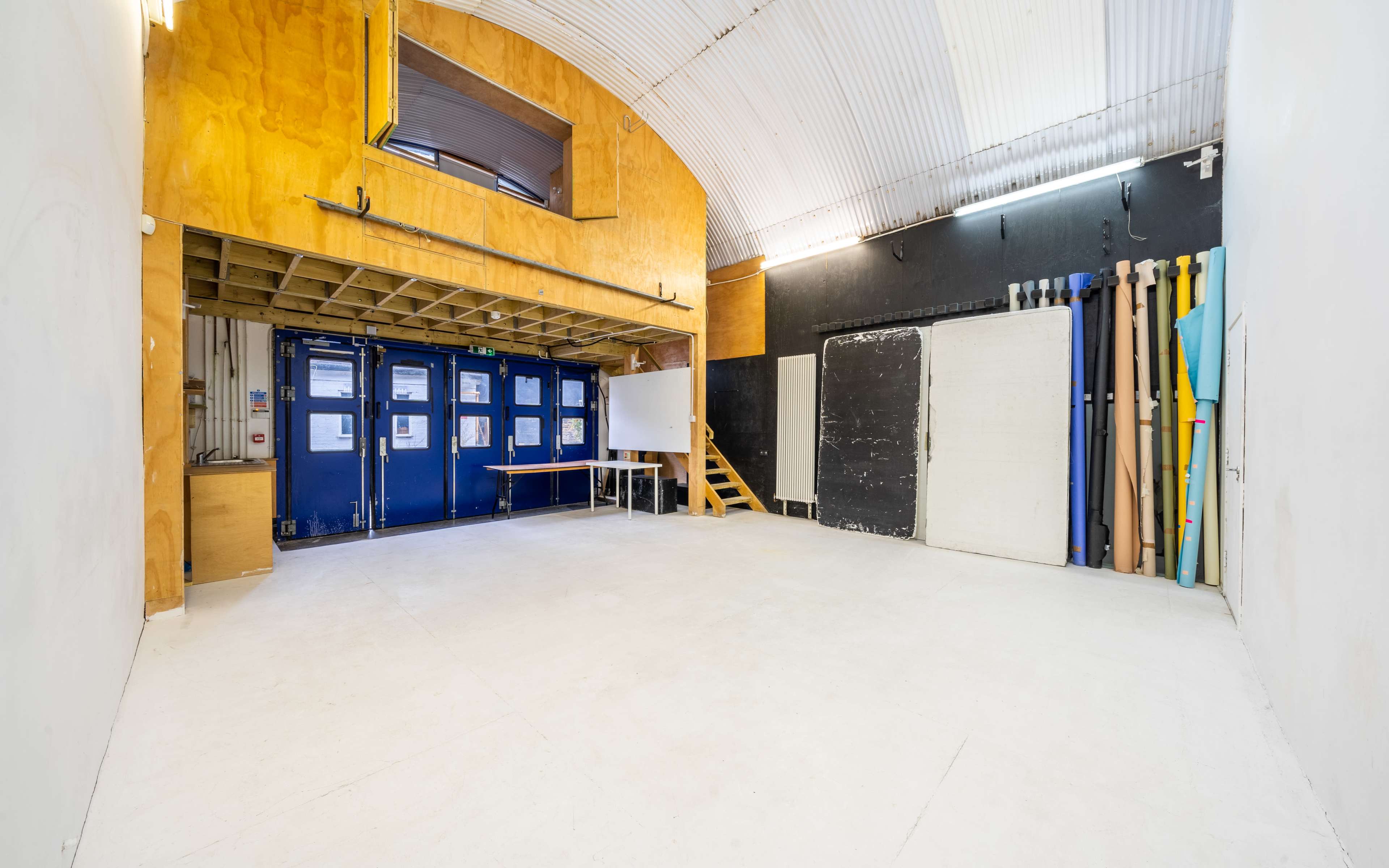 A spacious, empty studio room with wooden paneling and various colored materials stored against the wall.