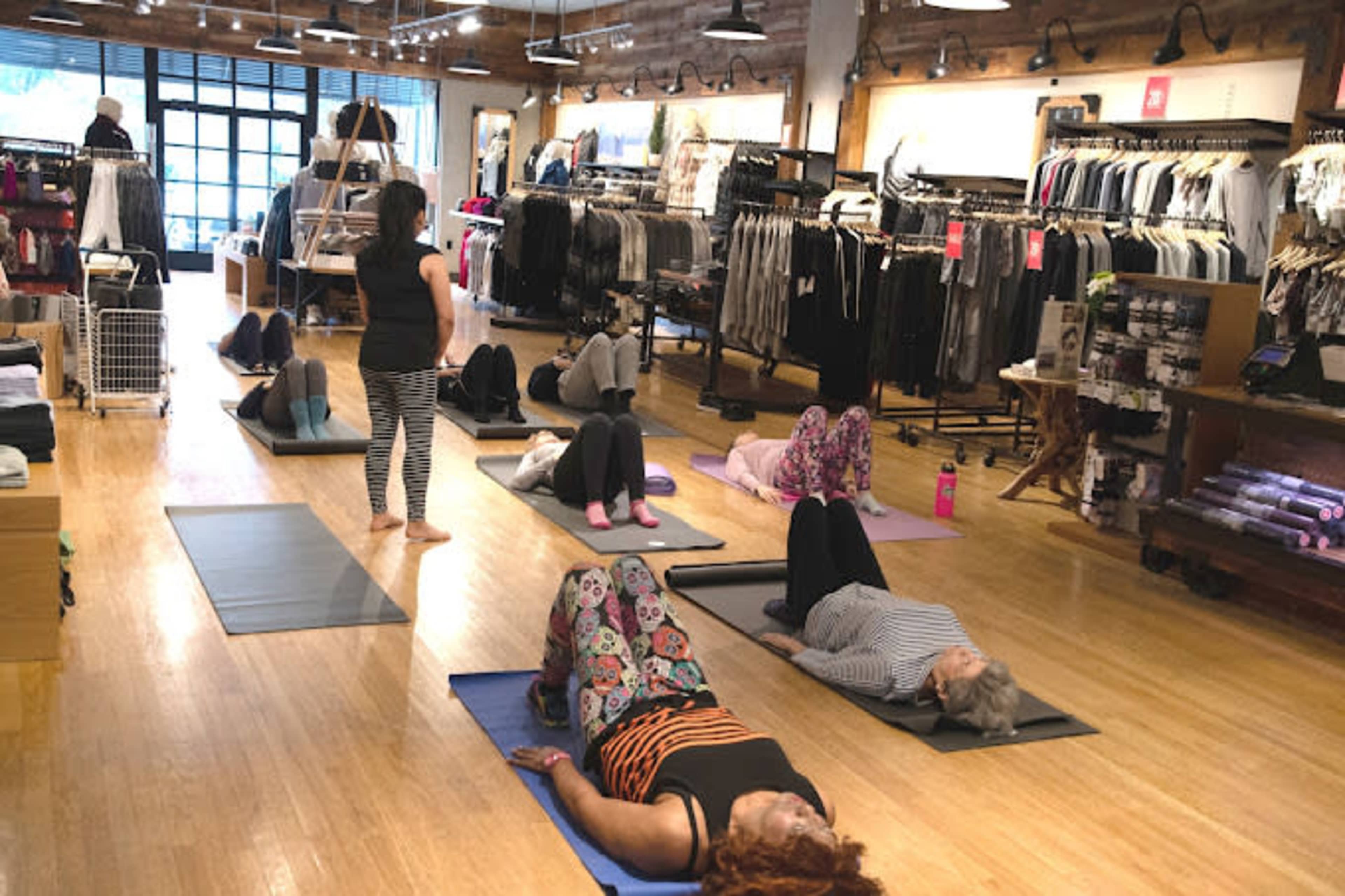 A group of people participate in a yoga class on mats inside a clothing store.