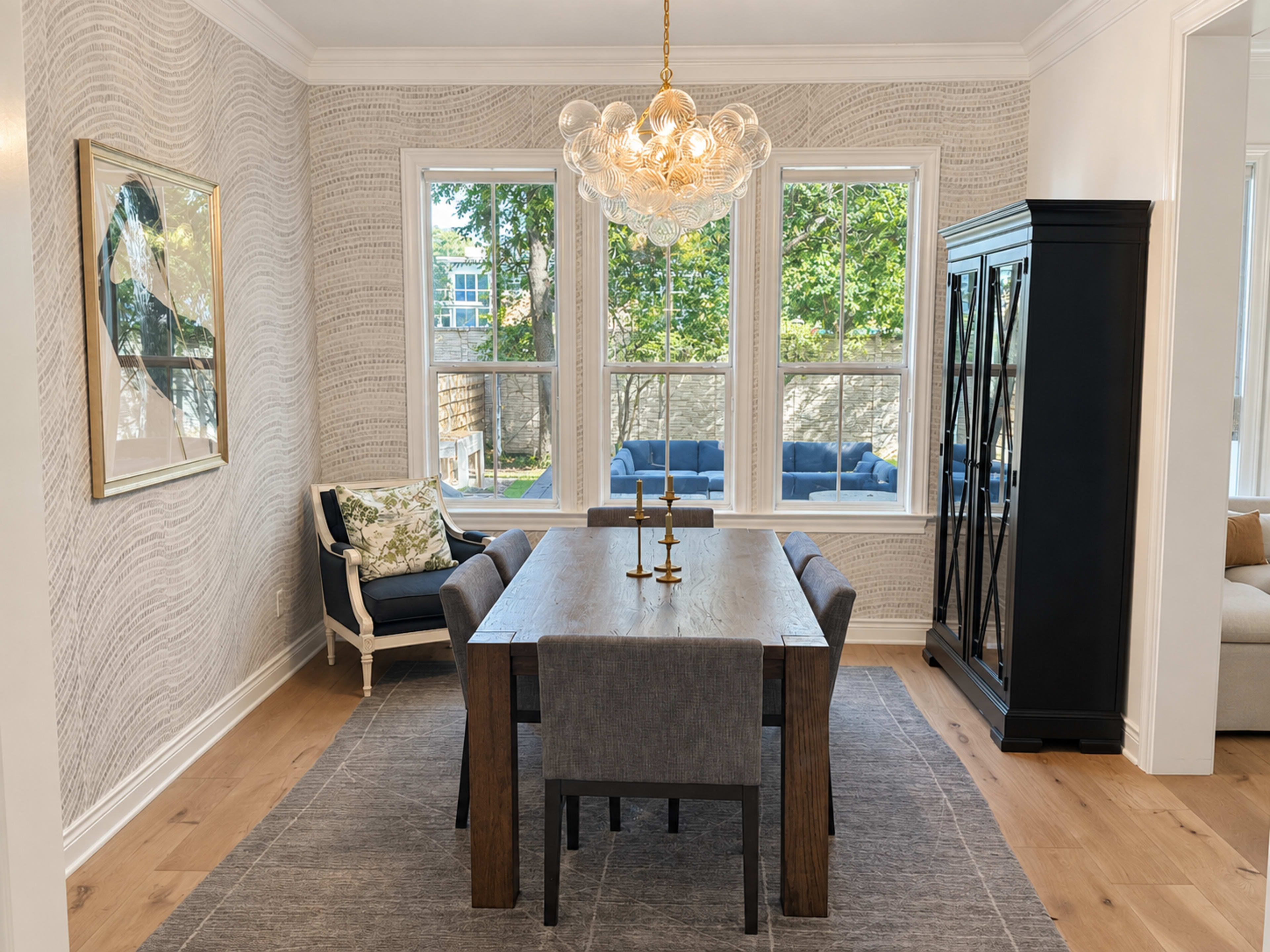 The dining area features a wooden table with gray upholstered chairs, surrounded by light-colored walls and large windows that allow natural light to fill the space.