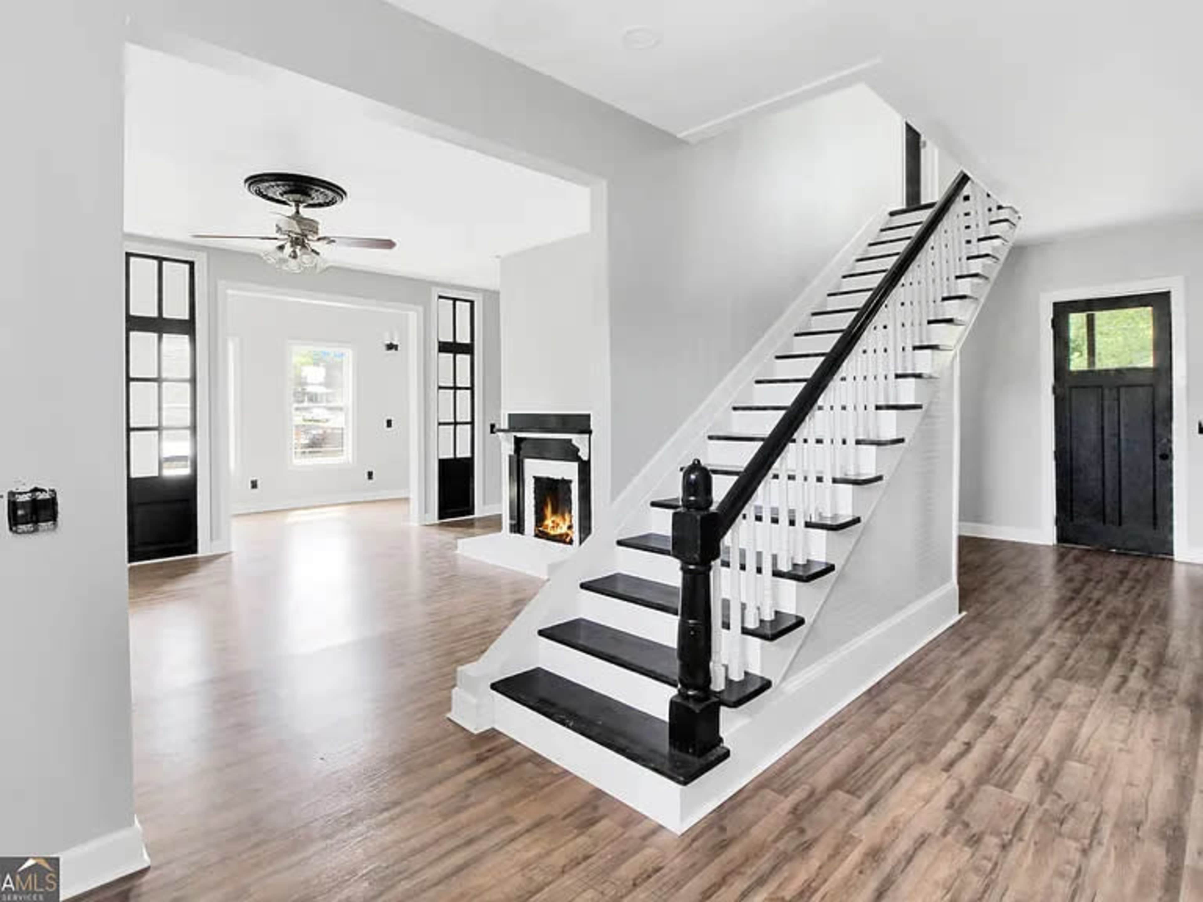 A modern interior showcases a staircase with black railings, a fireplace, and an open layout with light-colored walls and hardwood floors.