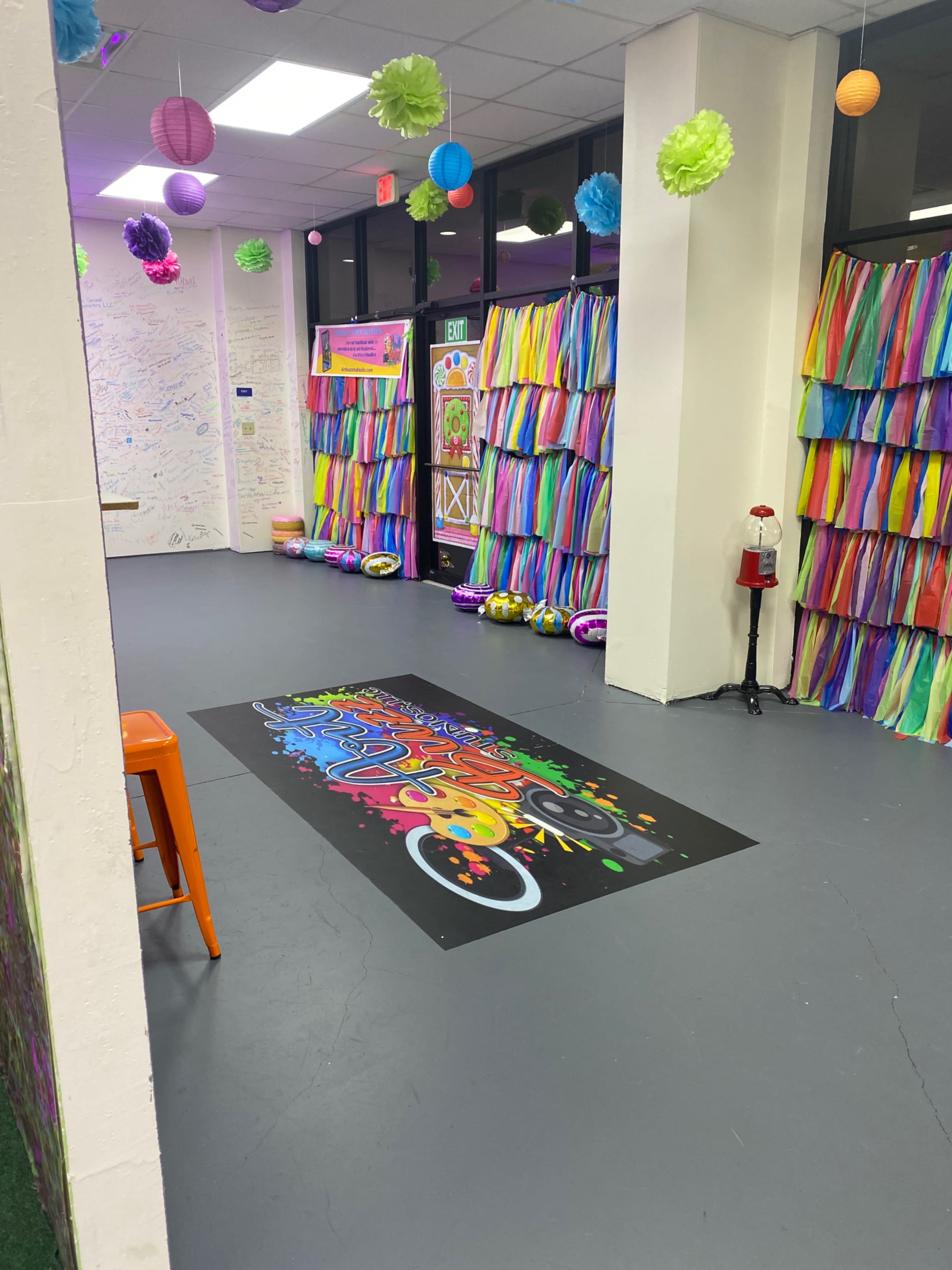 A colorful hallway decorated with streamers and paper flowers, featuring a vibrant floor mural in the center.