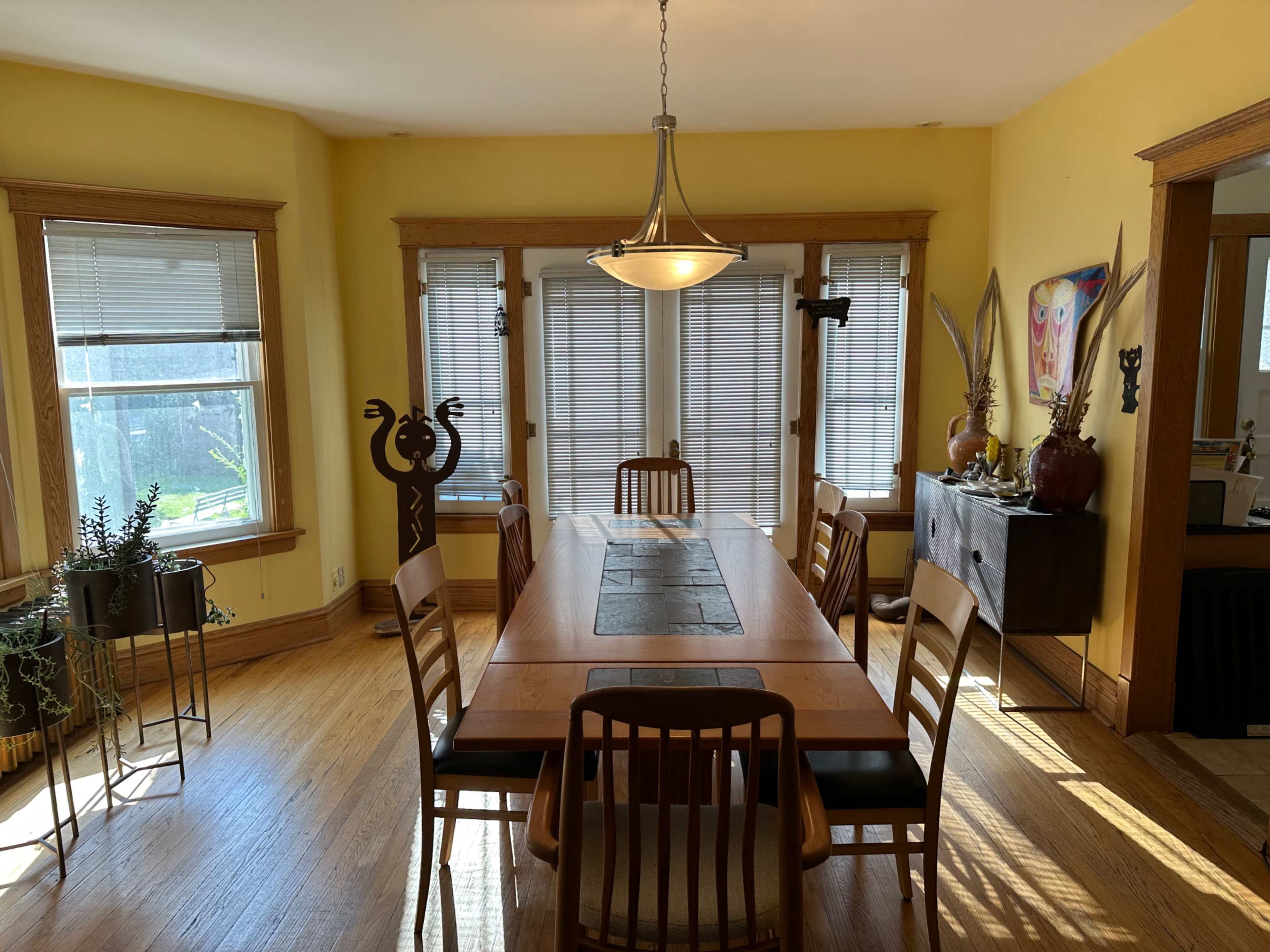 A spacious dining room features a long wooden table surrounded by chairs, with large windows allowing natural light to illuminate the space.