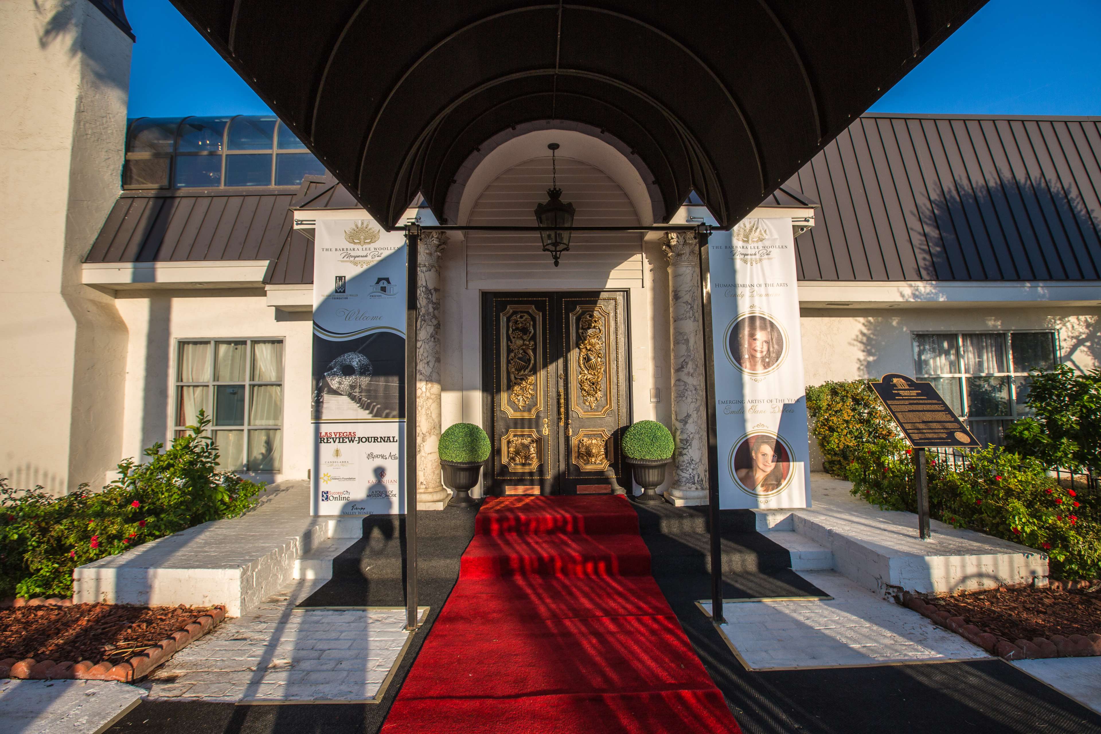 The entrance features a red carpet leading to a grand doorway adorned with ornate gold decorations and flanked by potted plants.