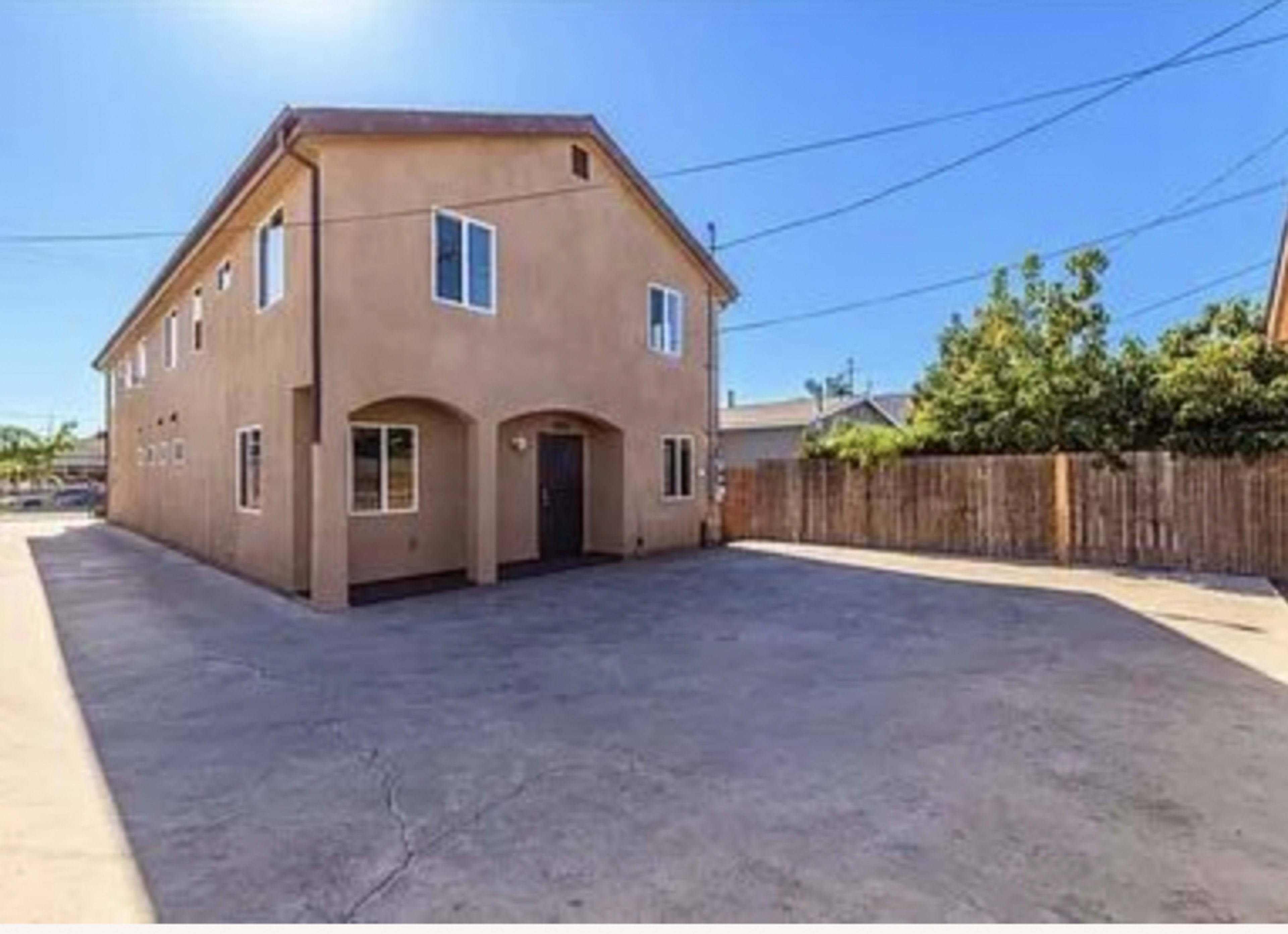 A two-story beige building with multiple windows and a fenced outdoor area is shown in a clear, blue sky.