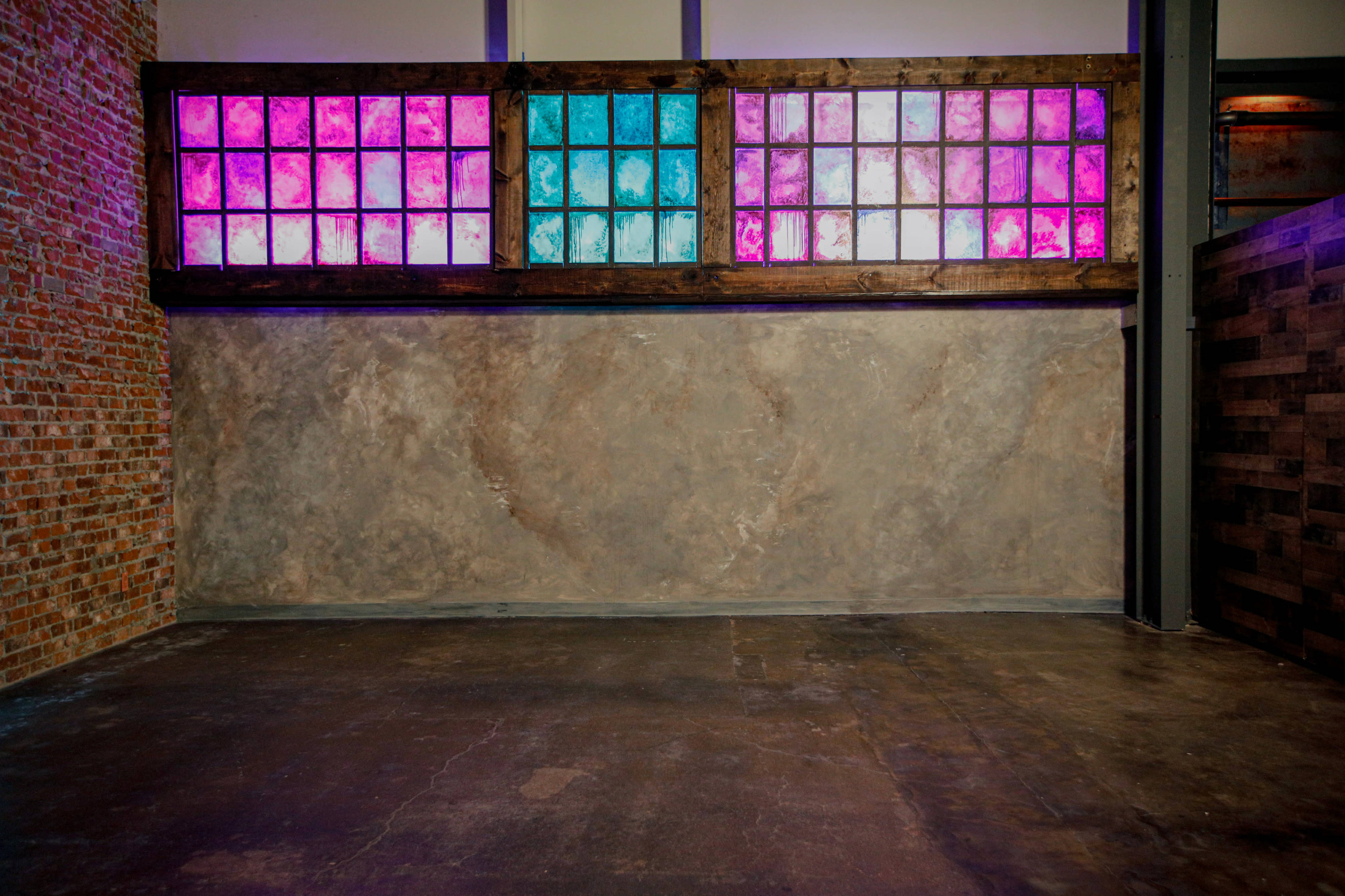 The image shows an industrial interior space with a textured wall and a feature wall made of colorful glass panels in shades of pink and blue.