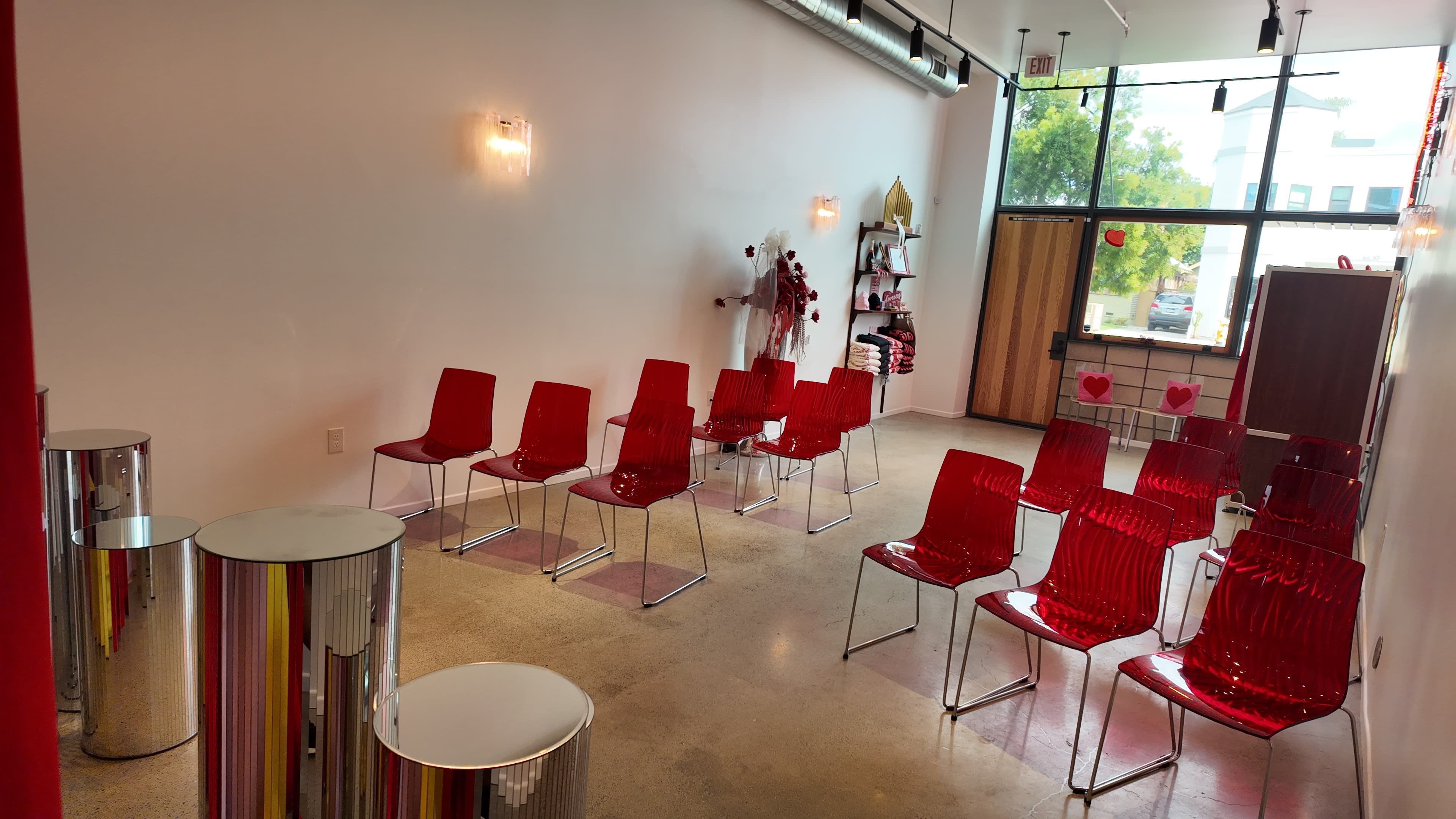 A waiting area with red transparent chairs arranged in rows, flanked by metallic tables and decorated with minimalistic wall fixtures.