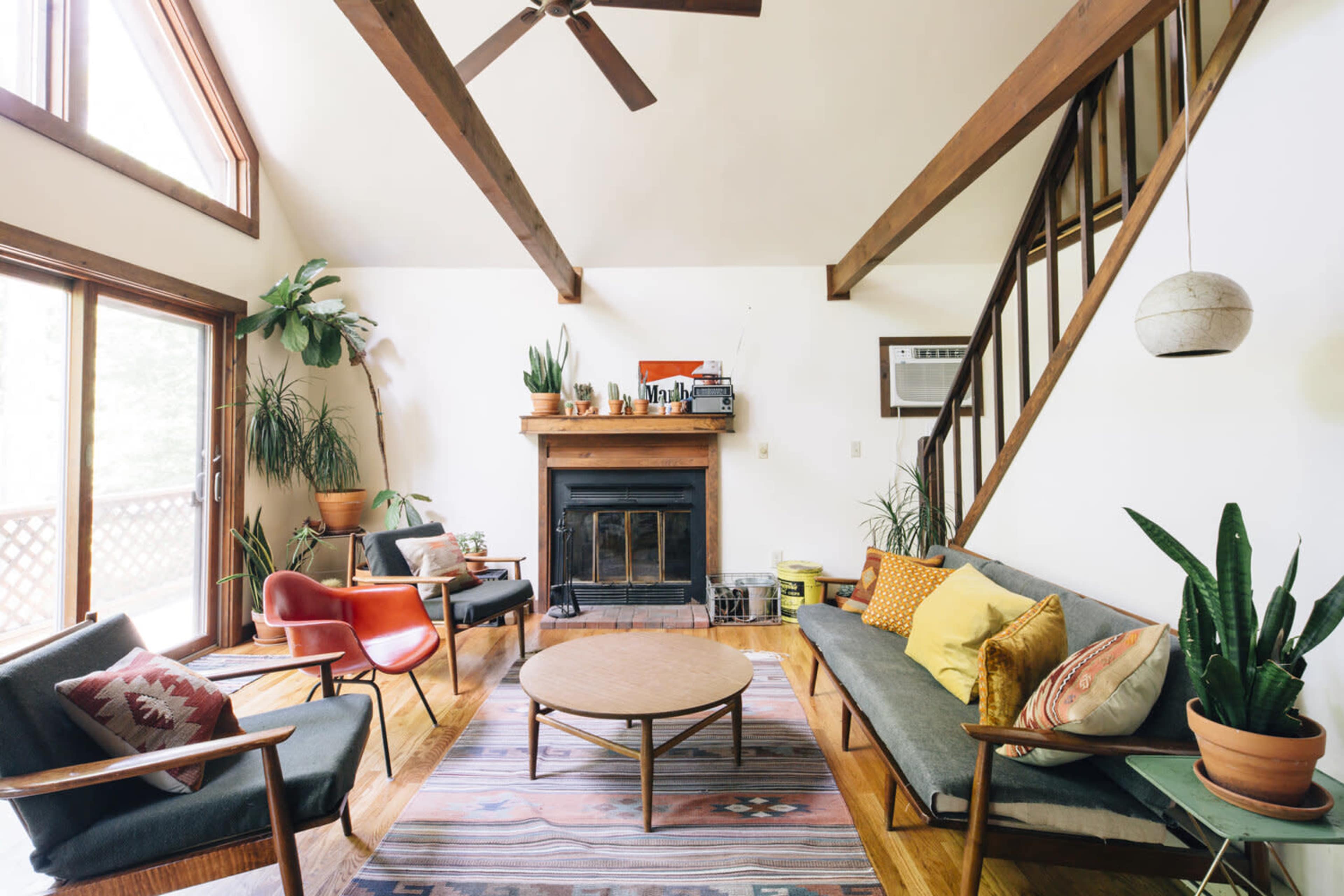 The image shows a modern living room featuring two sofas, a coffee table, a fireplace, and large windows with natural light.
