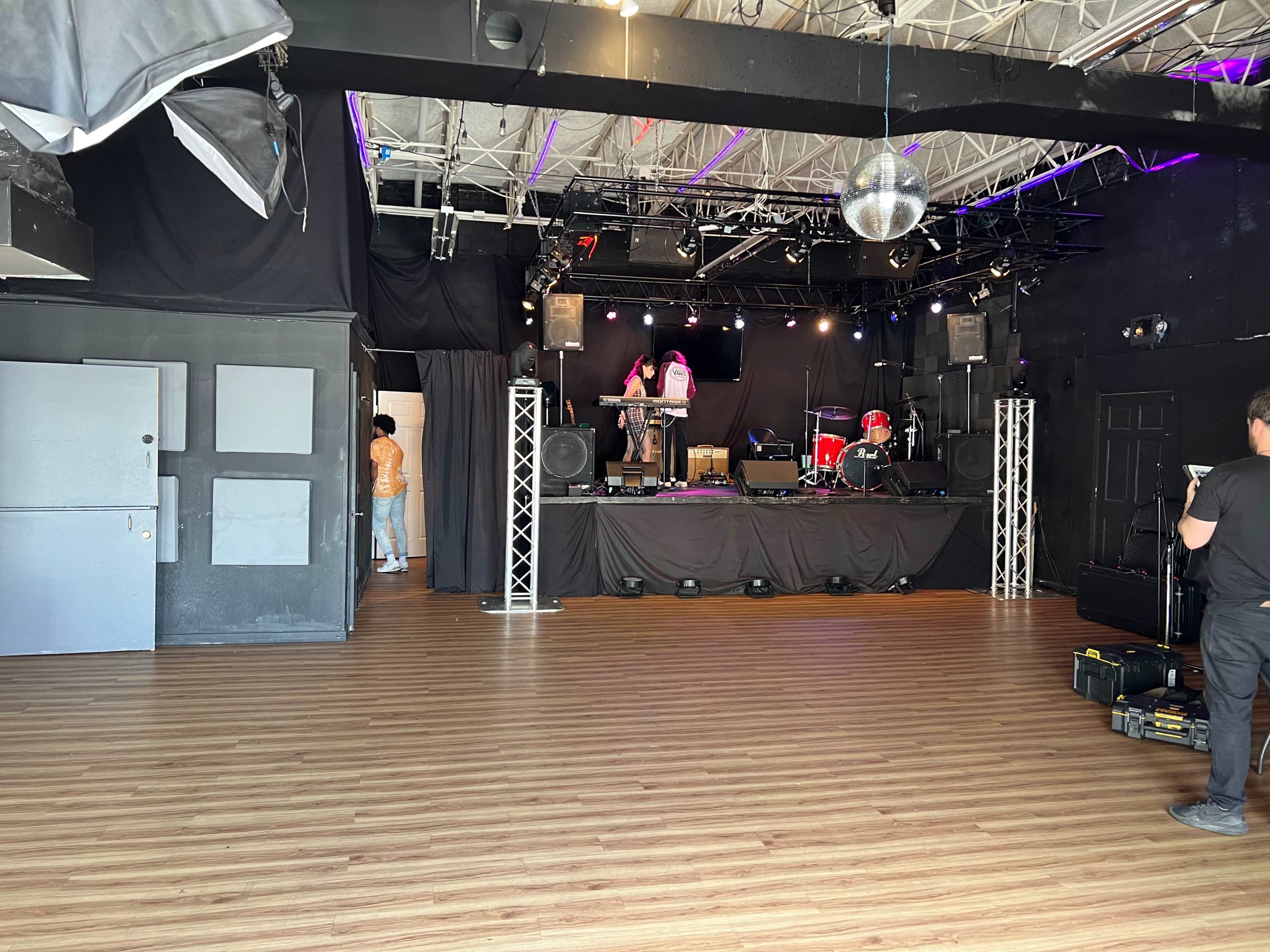 A performance stage set up in a venue with empty flooring and sound equipment in the foreground.