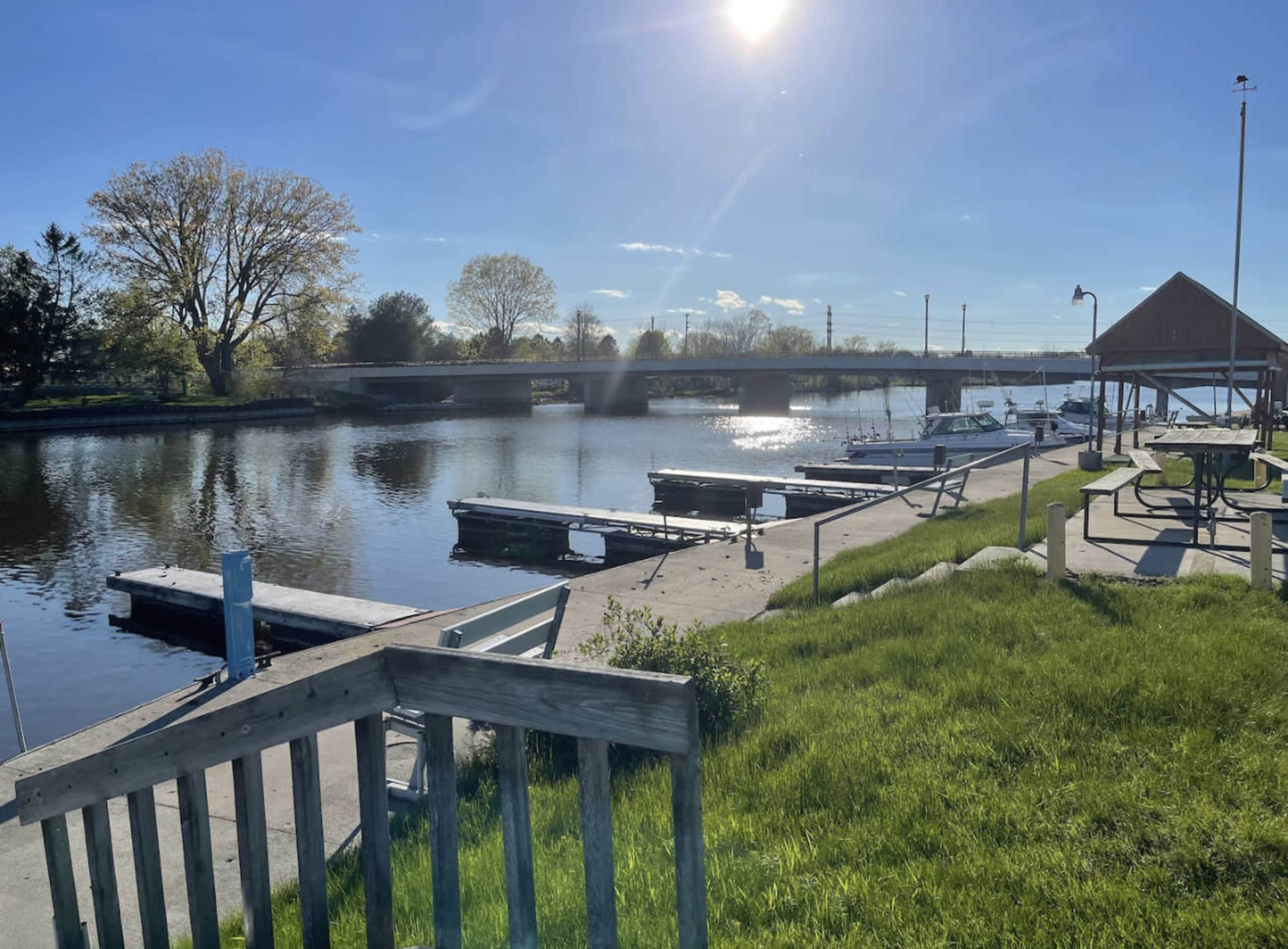 A calm river scene with several boats docked next to a grassy area under a clear blue sky.