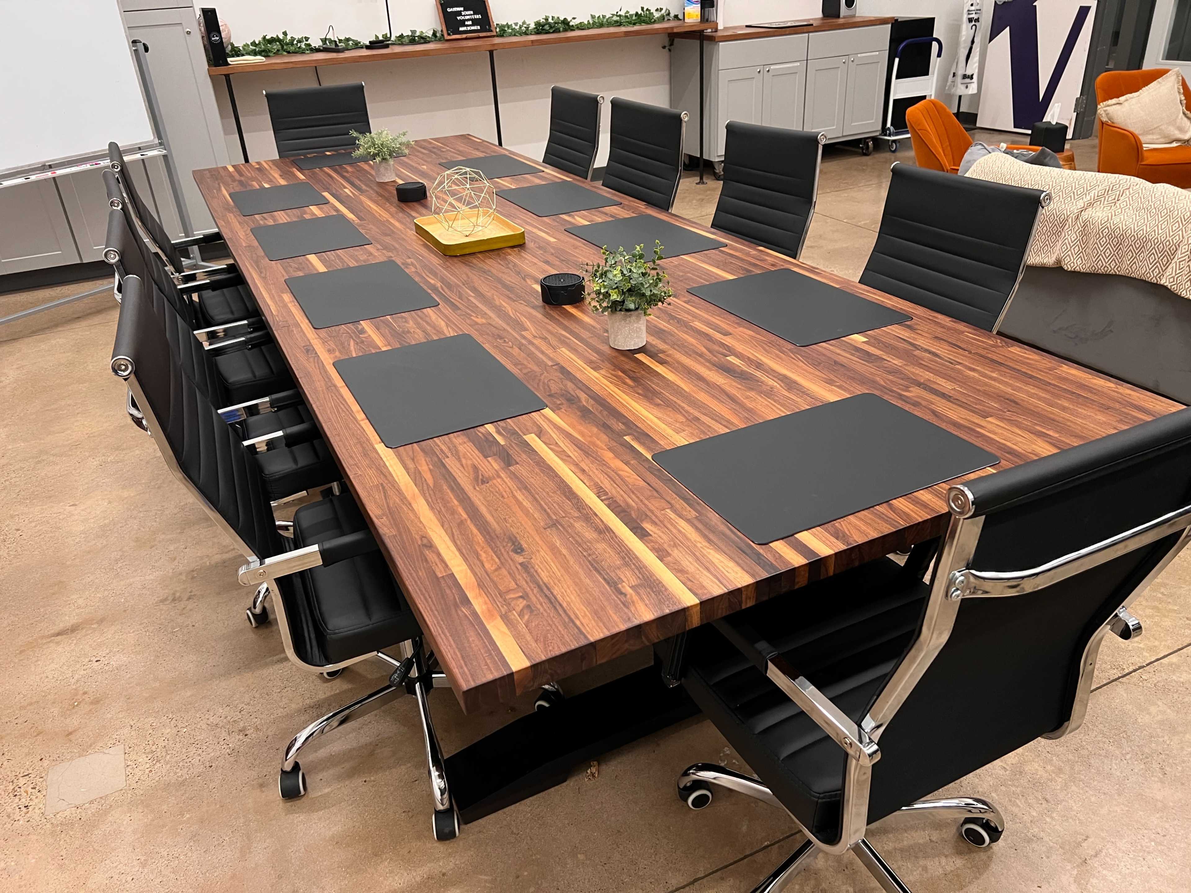 A long wooden conference table is surrounded by black ergonomic chairs in a modern meeting room.