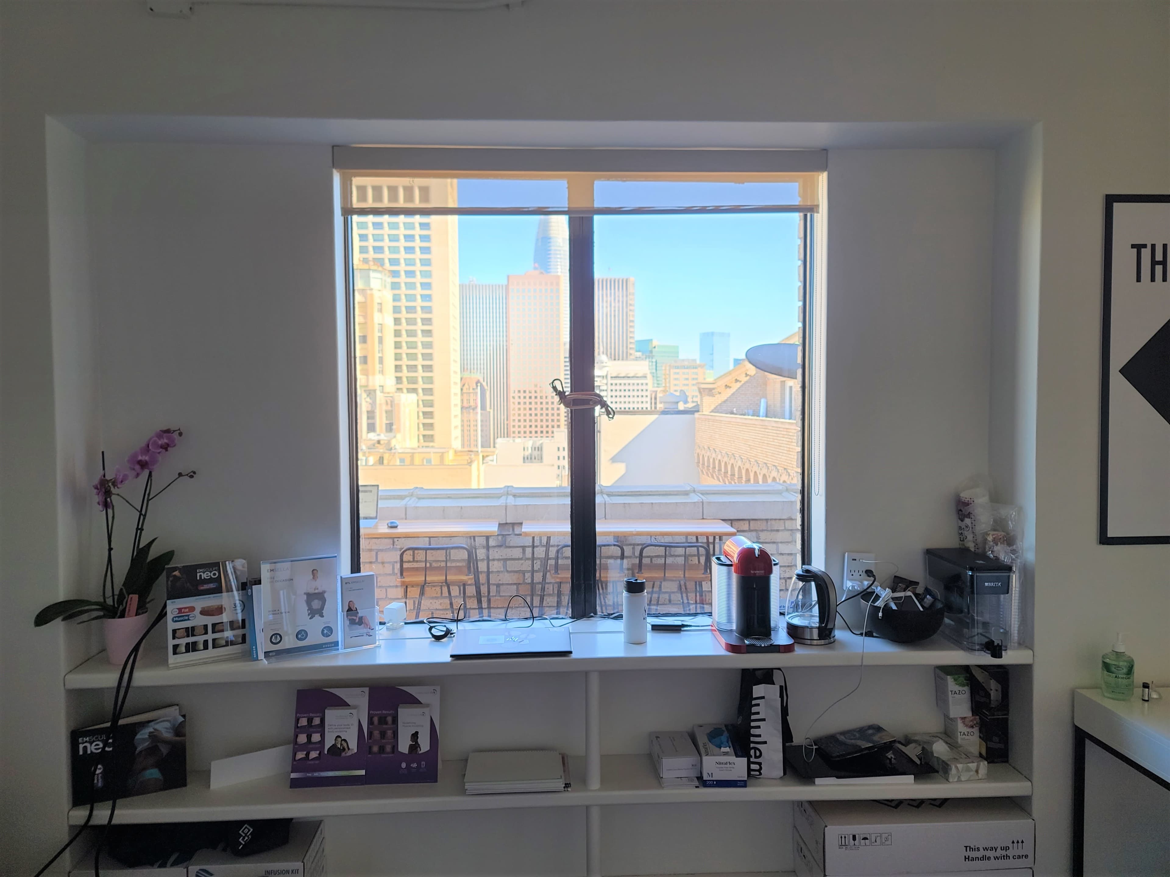 A window view of a city skyline with various office items arranged on a shelf beneath the window.