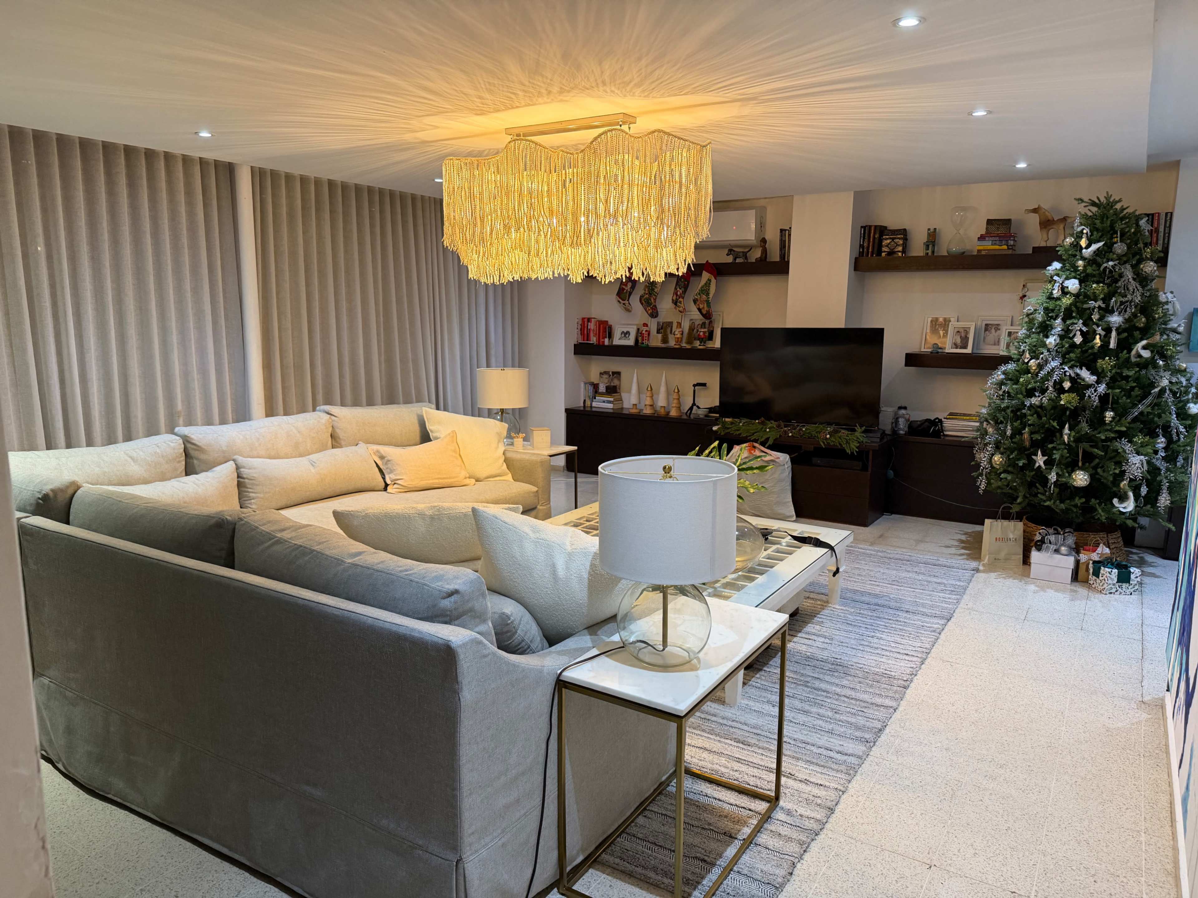 The image shows a modern living room with a large sectional sofa, a flat-screen TV mounted on the wall, and a decorated Christmas tree in the corner.