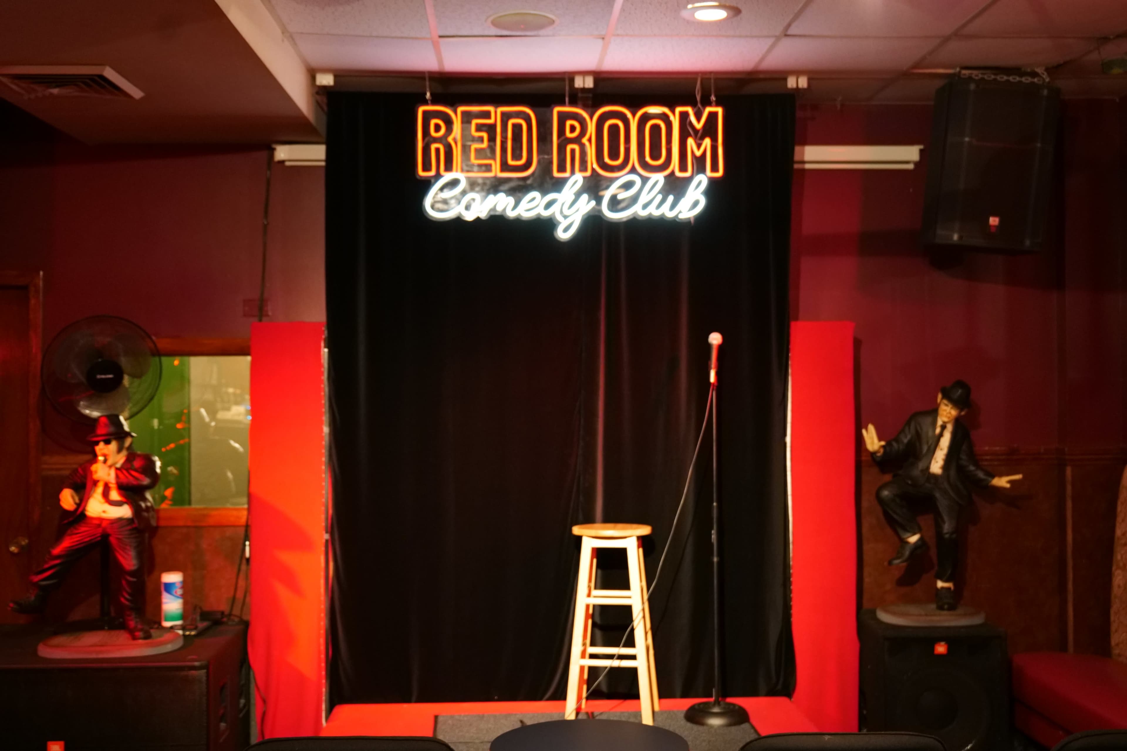 A stage setup at the Red Room Comedy Club, featuring a microphone on a stool and decorative statues on either side.