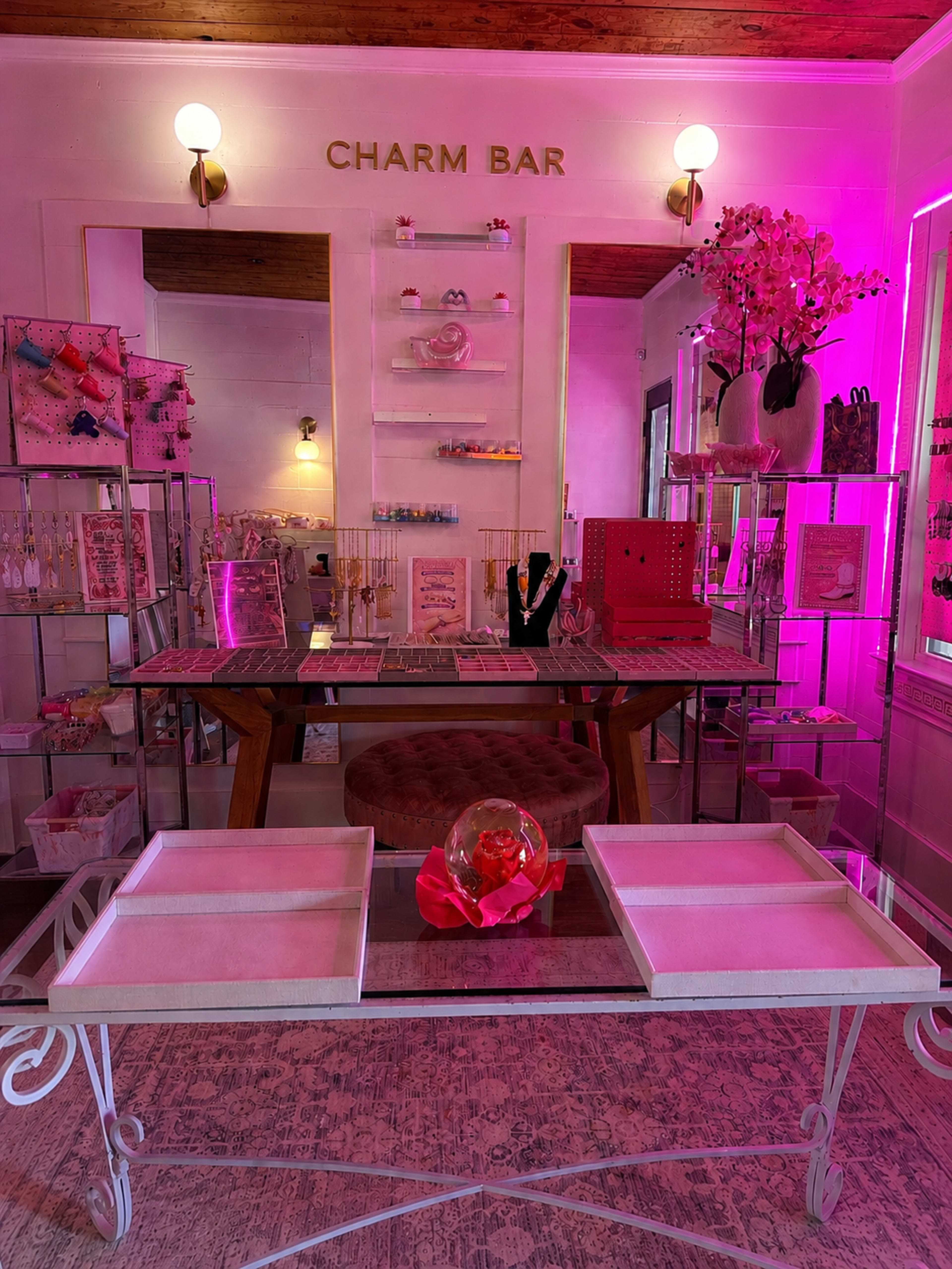 The image shows a brightly lit boutique space with a display area featuring jewelry, accessories, and decorative elements, all under a pink hue.