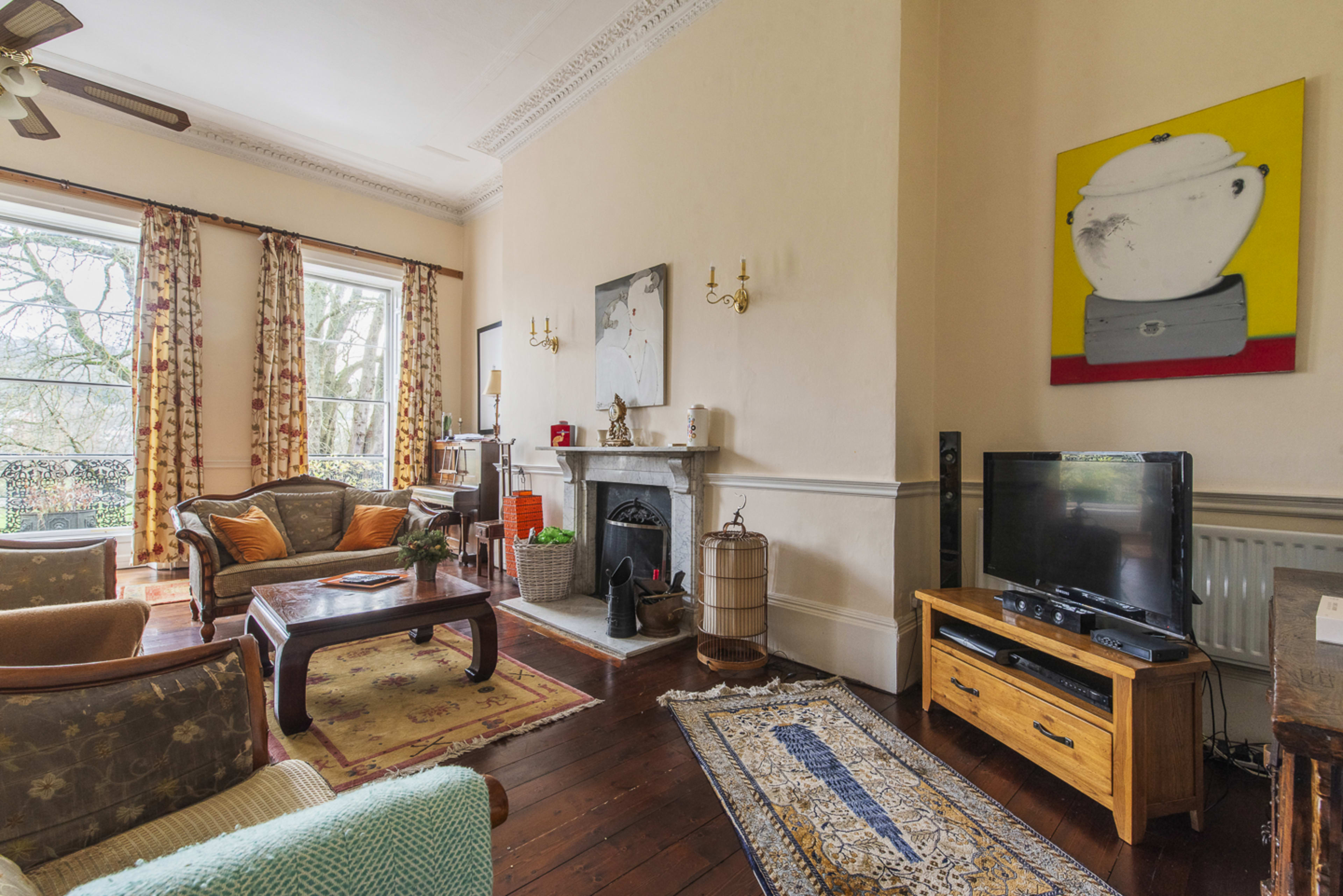 The image shows a living room with a mix of seating arrangements, a decorative fireplace, and a large window displaying trees outside.