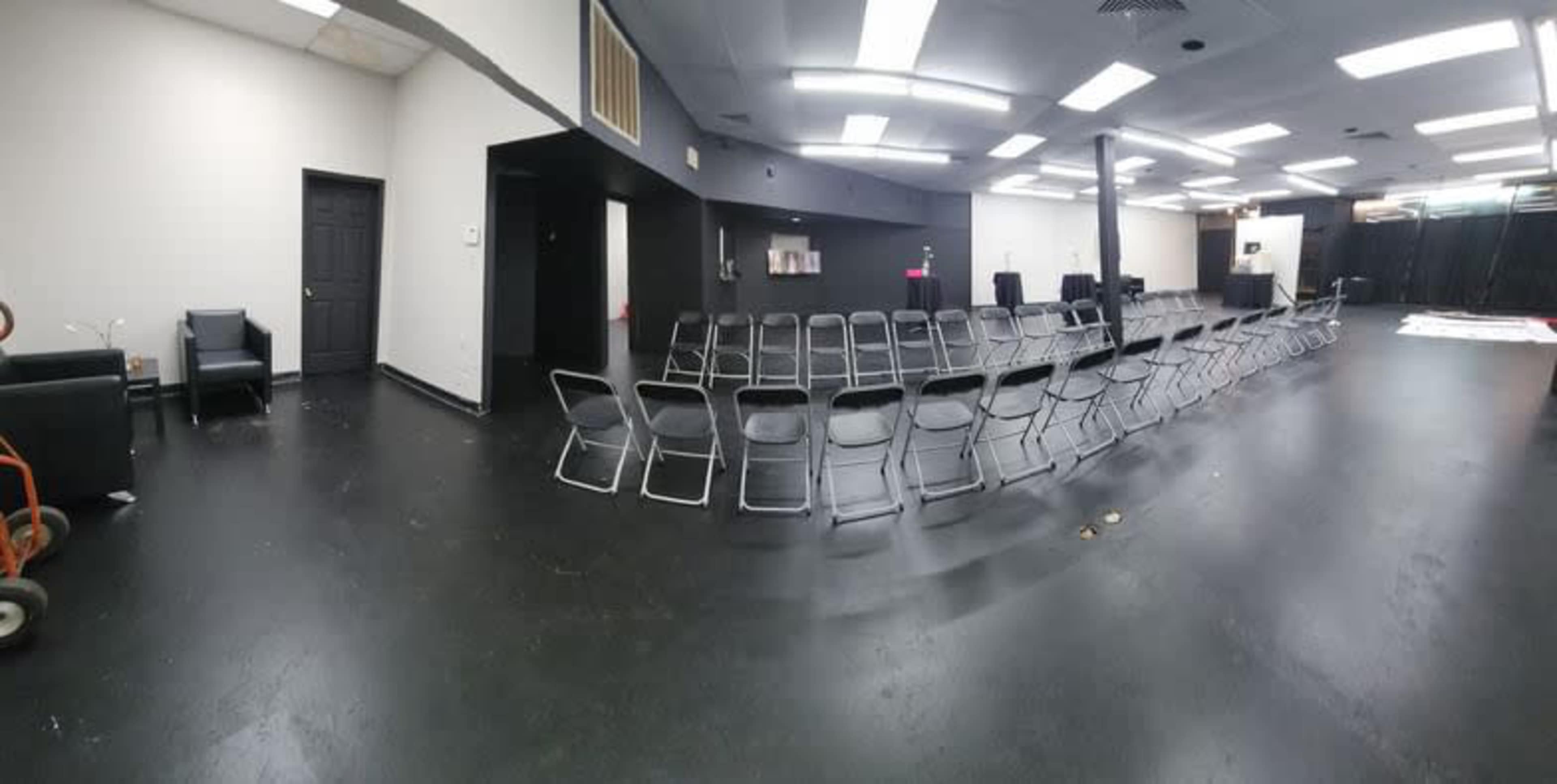 A spacious room with a row of folding chairs arranged in the center and minimal furniture along the walls.